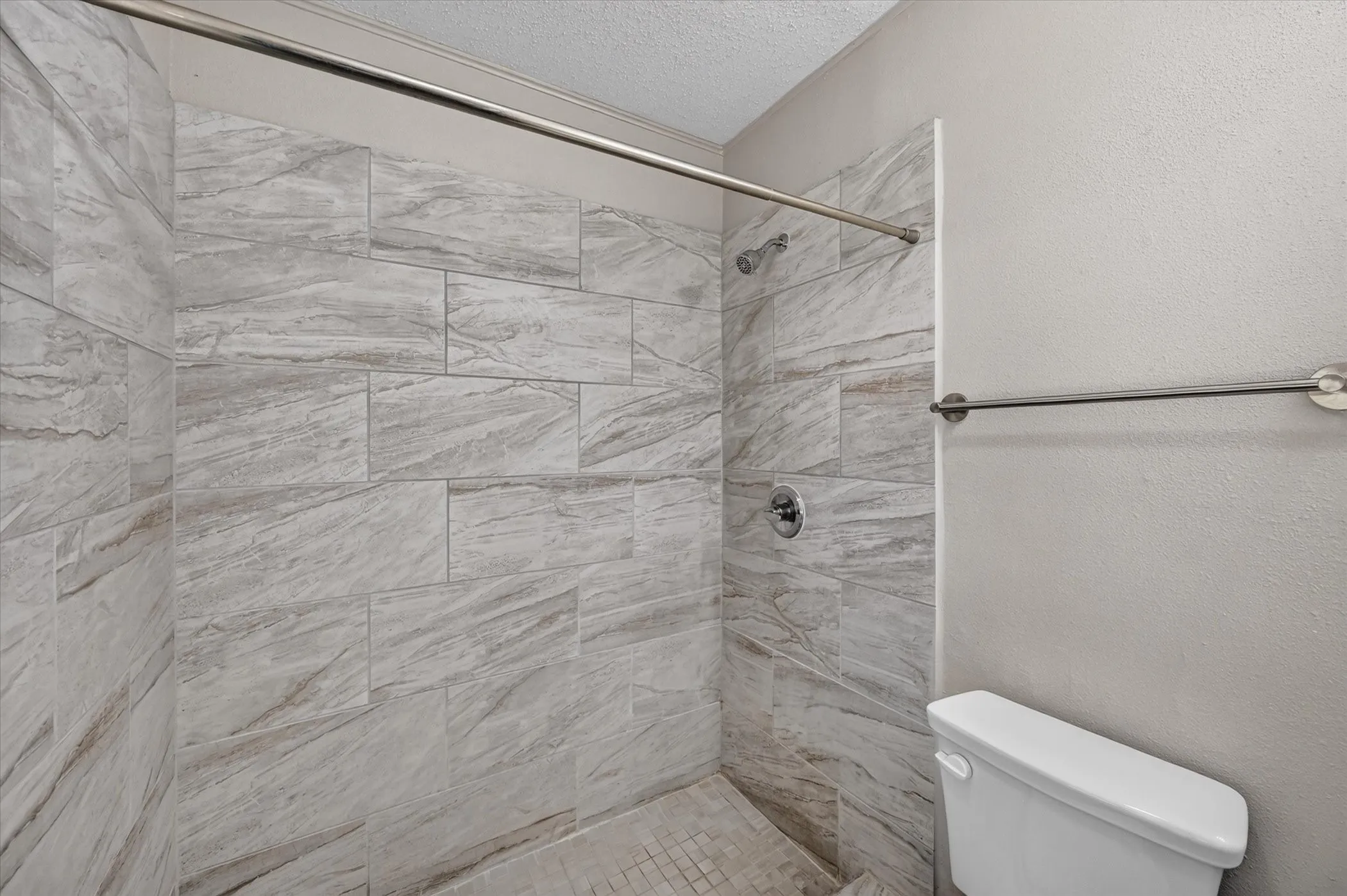 Shower with large-format stone-finish wall tile, chrome fixtures, and a white toilet