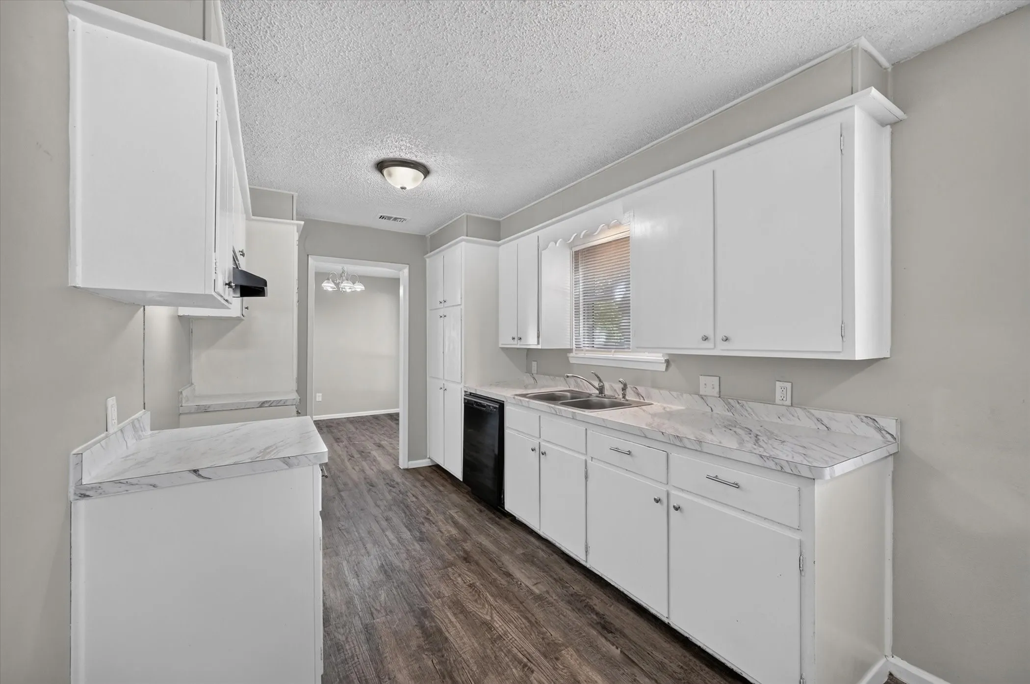 White cabinetry, wood-finish flooring, white countertops, built-in dishwasher, and a double basin sink with a chrome faucet
