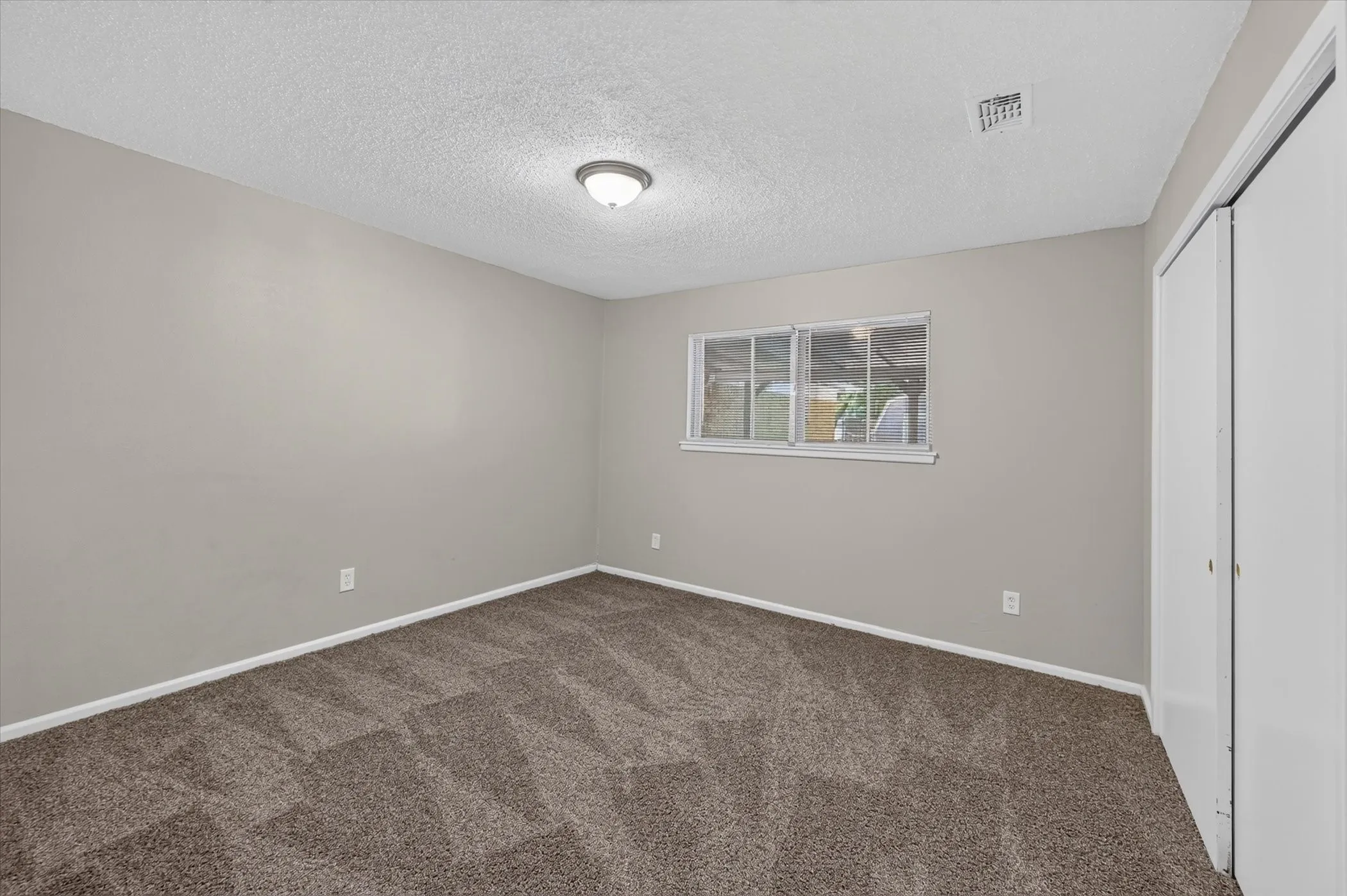 Neutral tone wall paint, textured ceiling, flush mount ceiling light fixture, window with white trim, and carpet flooring