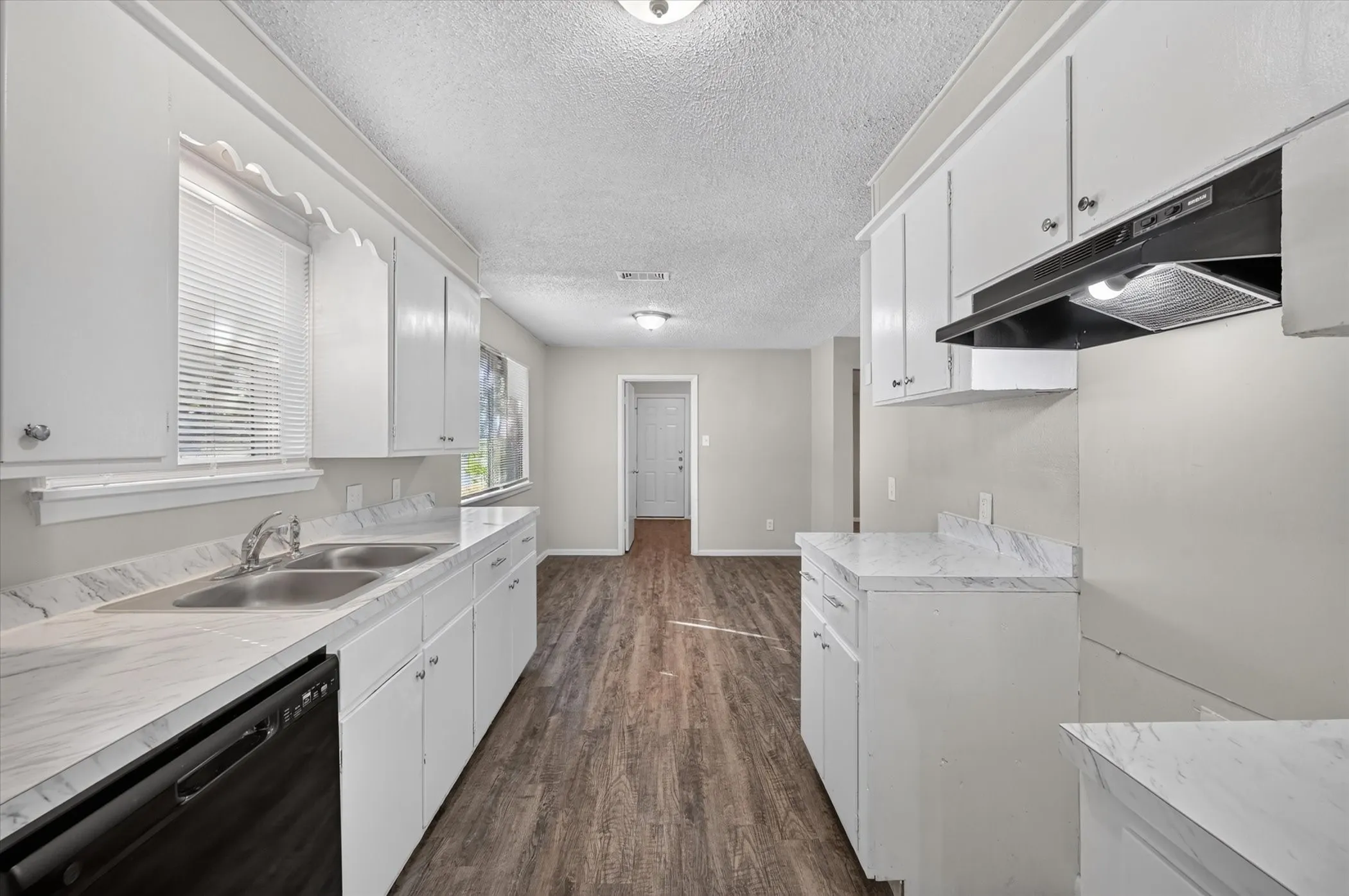 White cabinetry with decorative trim, dual basin stainless steel sink, black built-in dishwasher, black range hood, and wood-finish flooring