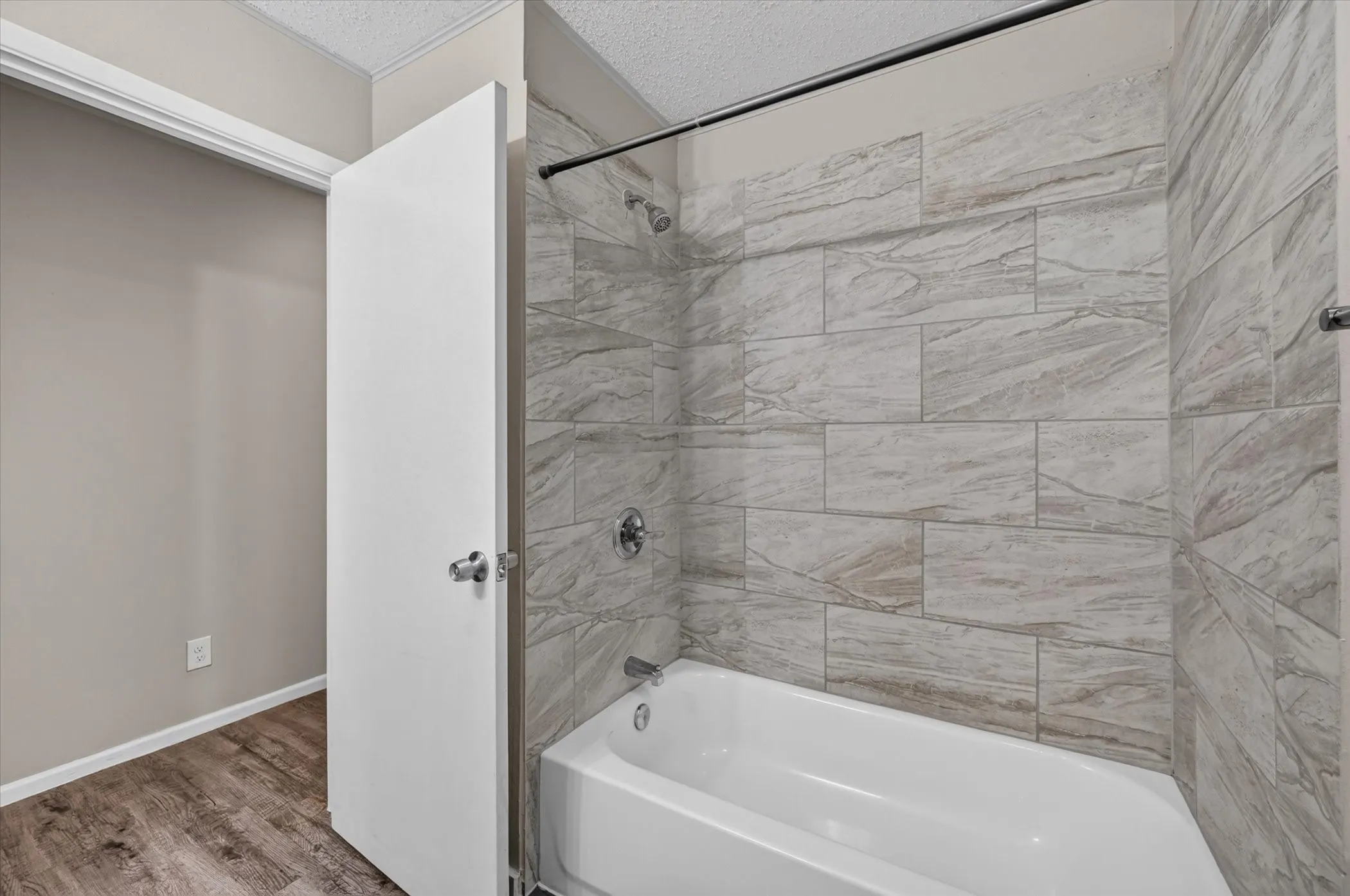 Bathtub and shower combination with large format tiled surround, chrome fixtures, and wood-finish flooring