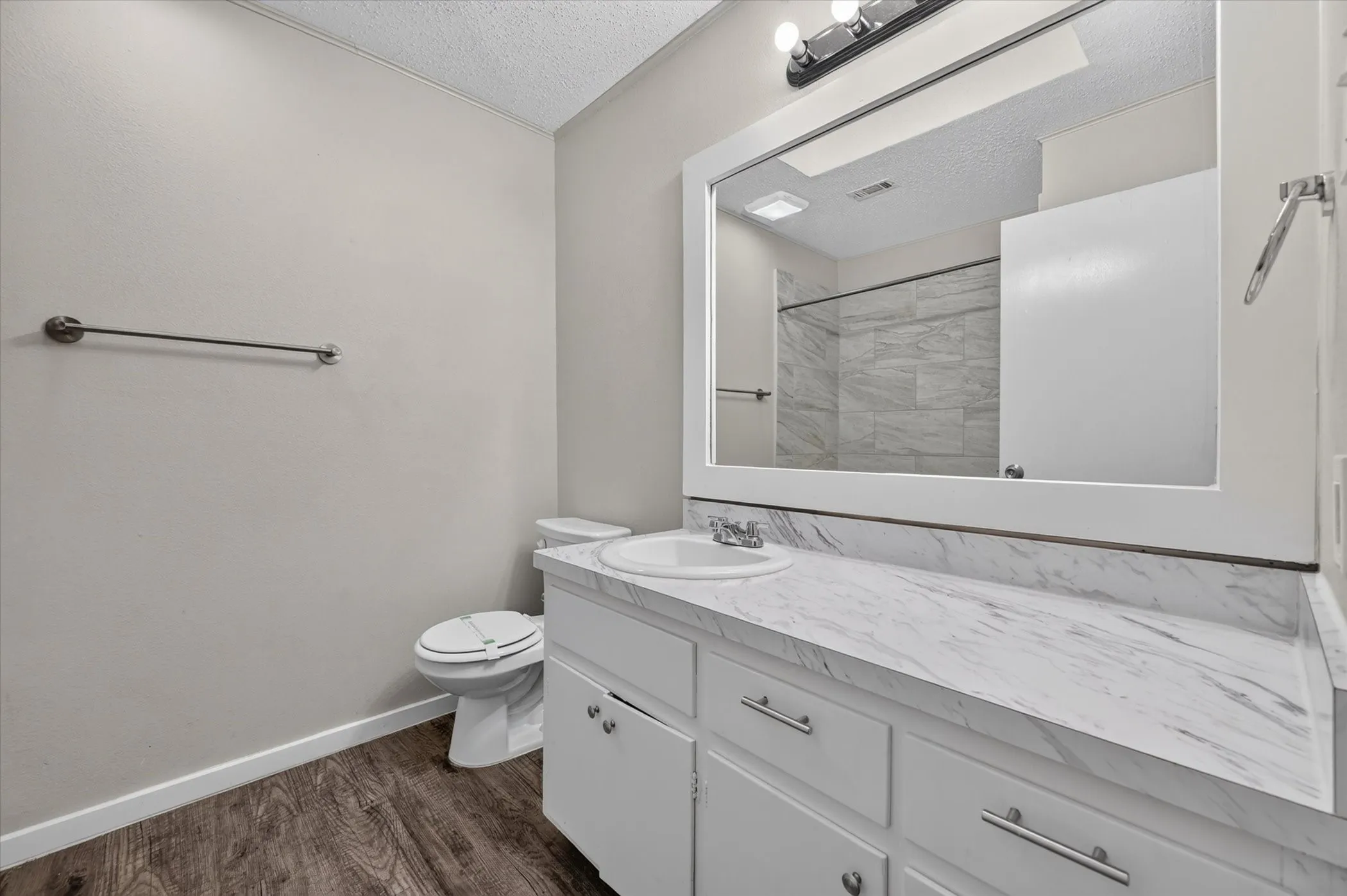 White vanity with a marble-patterned countertop, a rectangular mirror, and a chrome light fixture