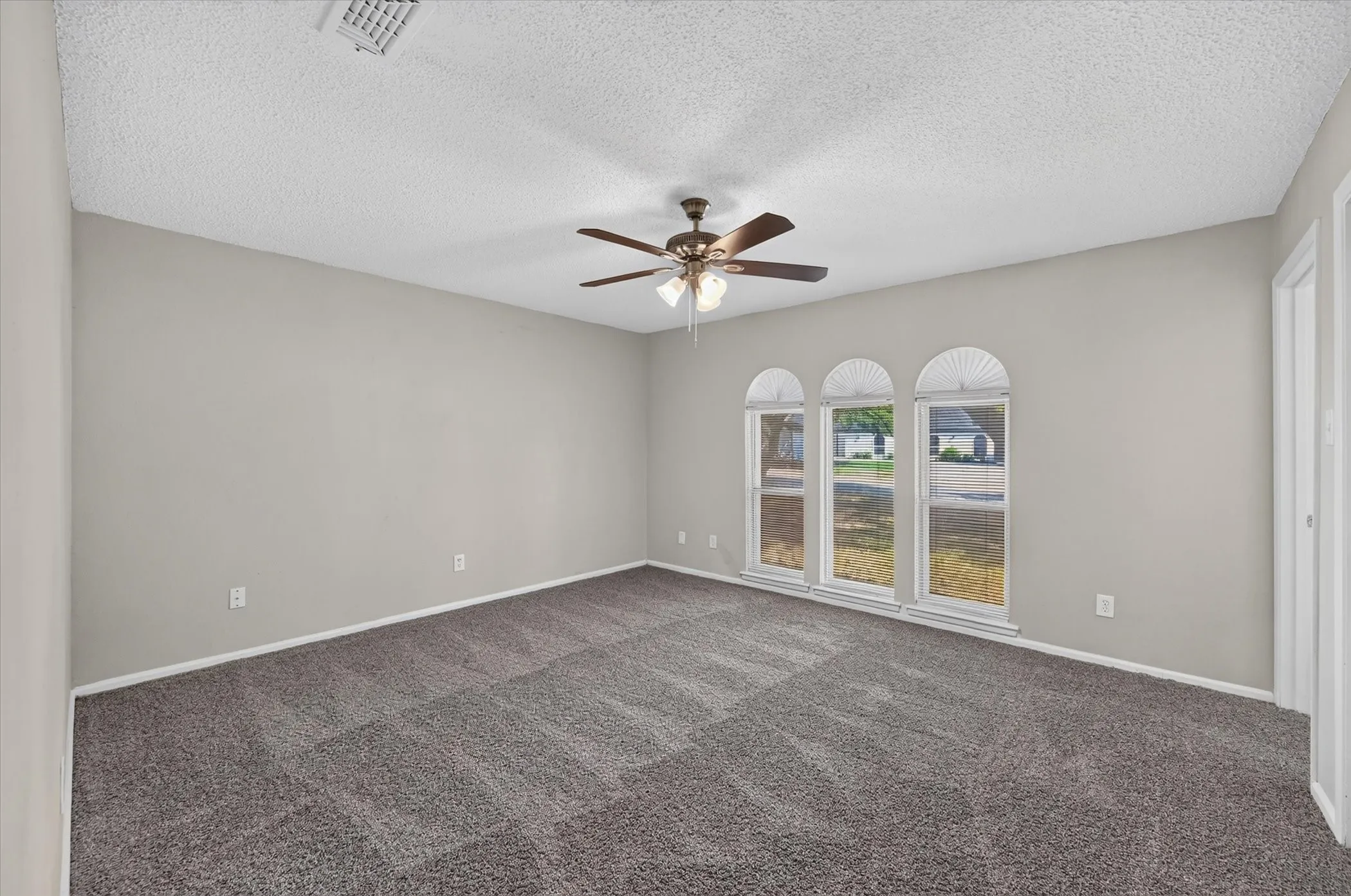 Spacious room featuring carpeting, light gray wall finishes, a ceiling fan with integrated lighting, and three arched-top windows