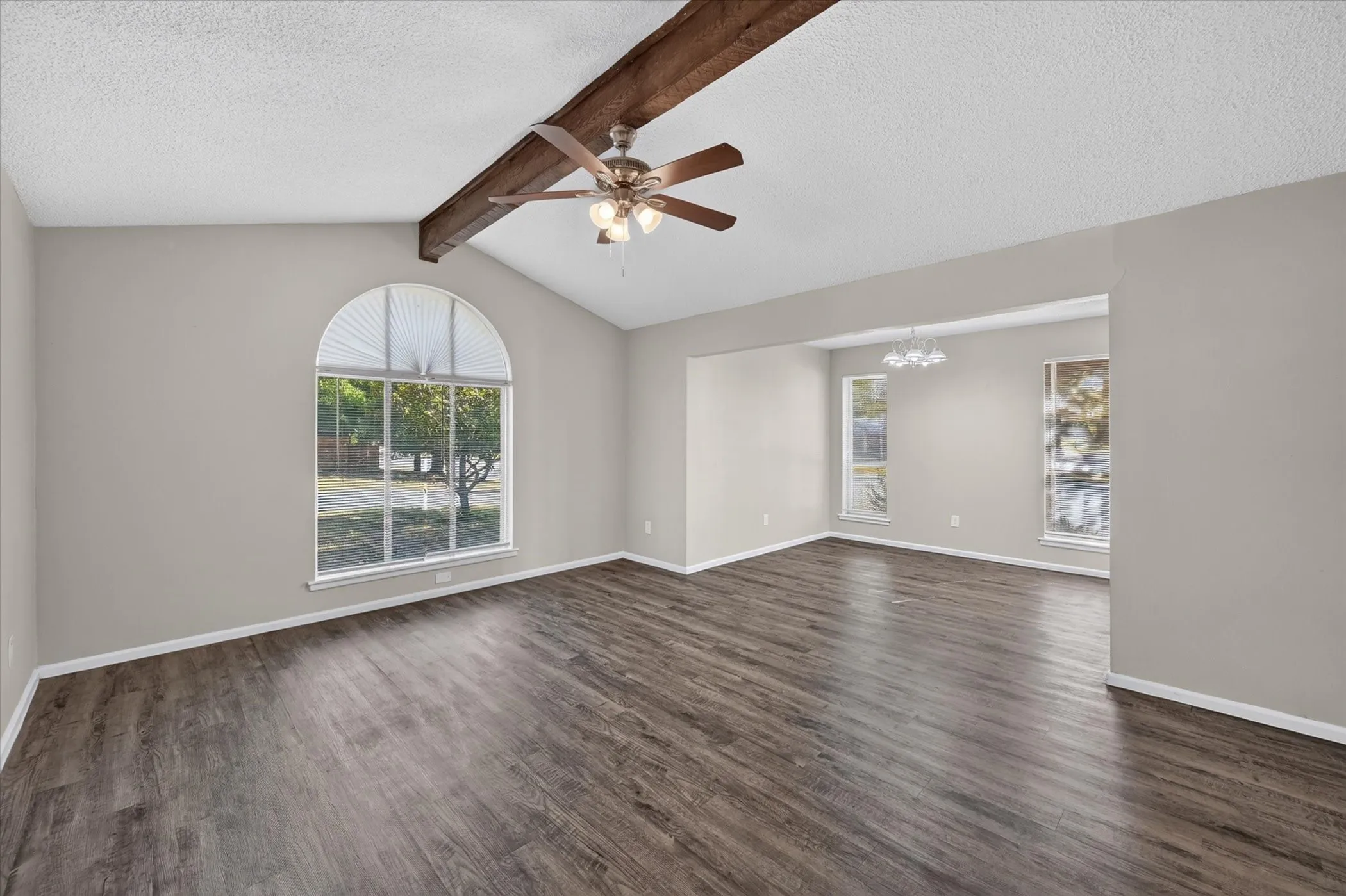 Vaulted ceiling with exposed wood beam, wood-finish flooring, arched window, and ceiling fan with integrated lighting