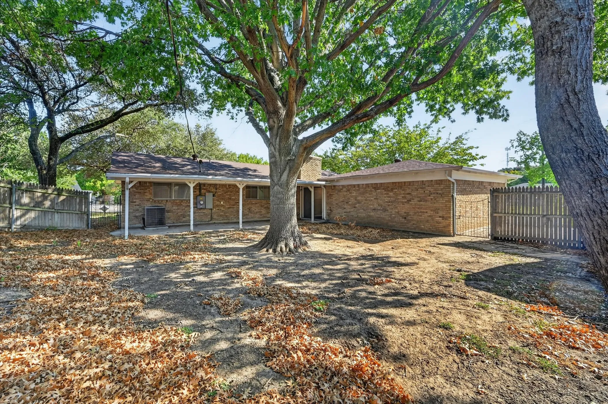 Brick exterior featuring a covered patio, a fenced perimeter, and mature trees