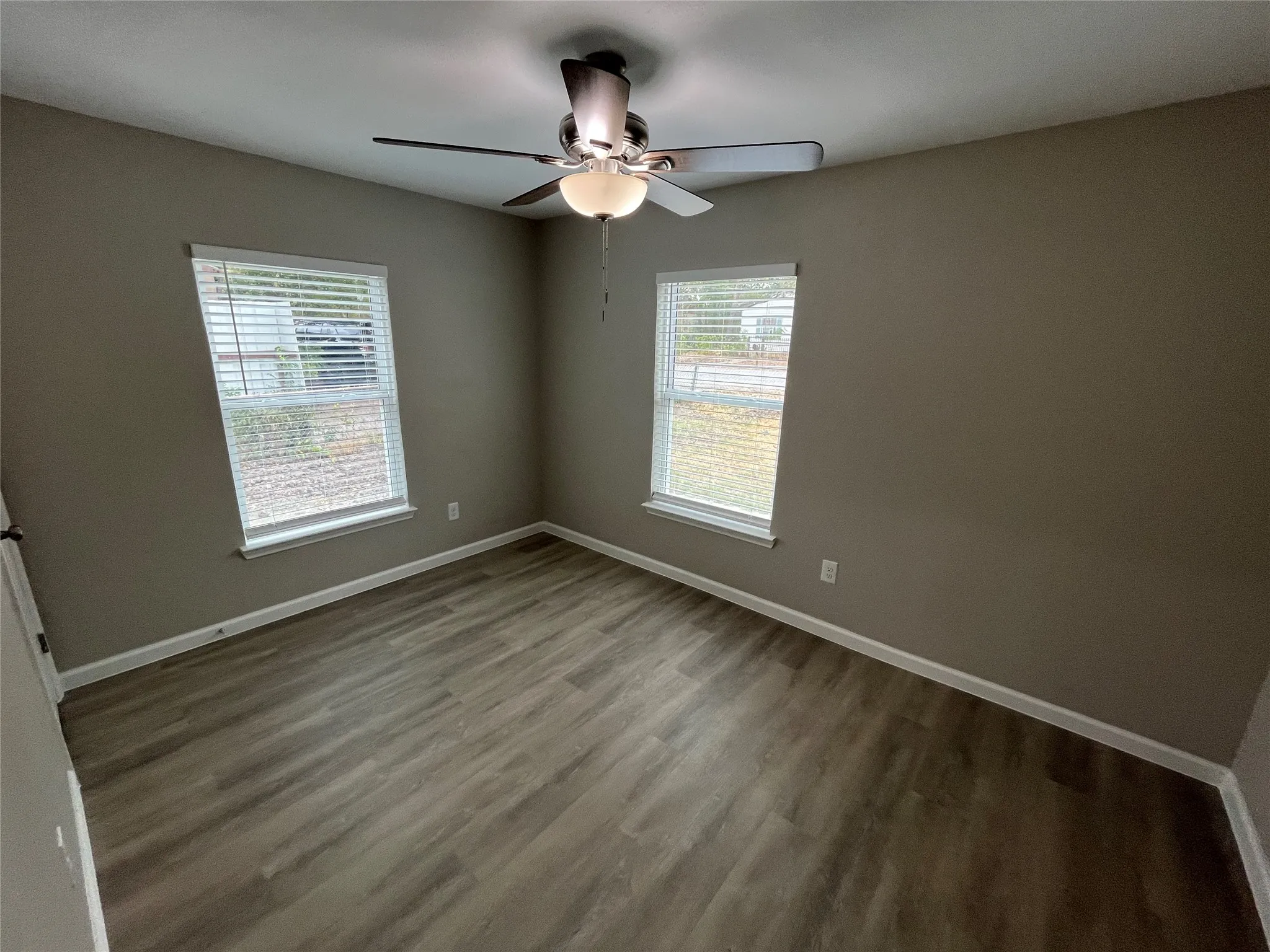 Room with neutral wall paint, wood-finish flooring, two windows with blinds, and a ceiling fan with integrated lighting