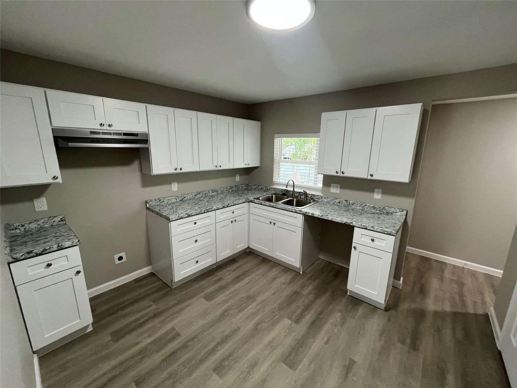 White shaker-style cabinetry, patterned countertops, stainless steel double basin sink, and wood-finish flooring