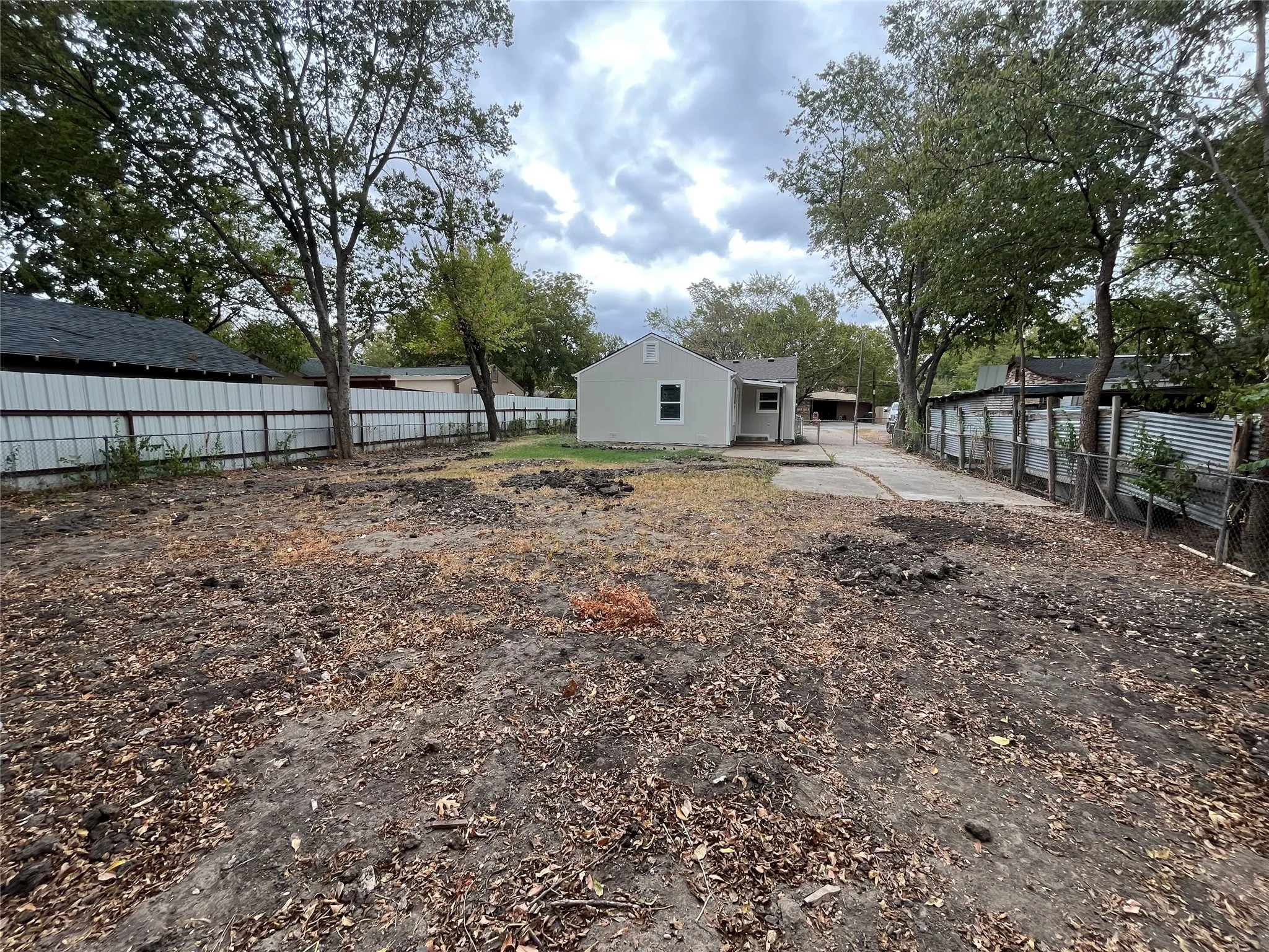 Expansive backyard space with mature trees, a detached structure, and a concrete driveway leading to the rear of the property