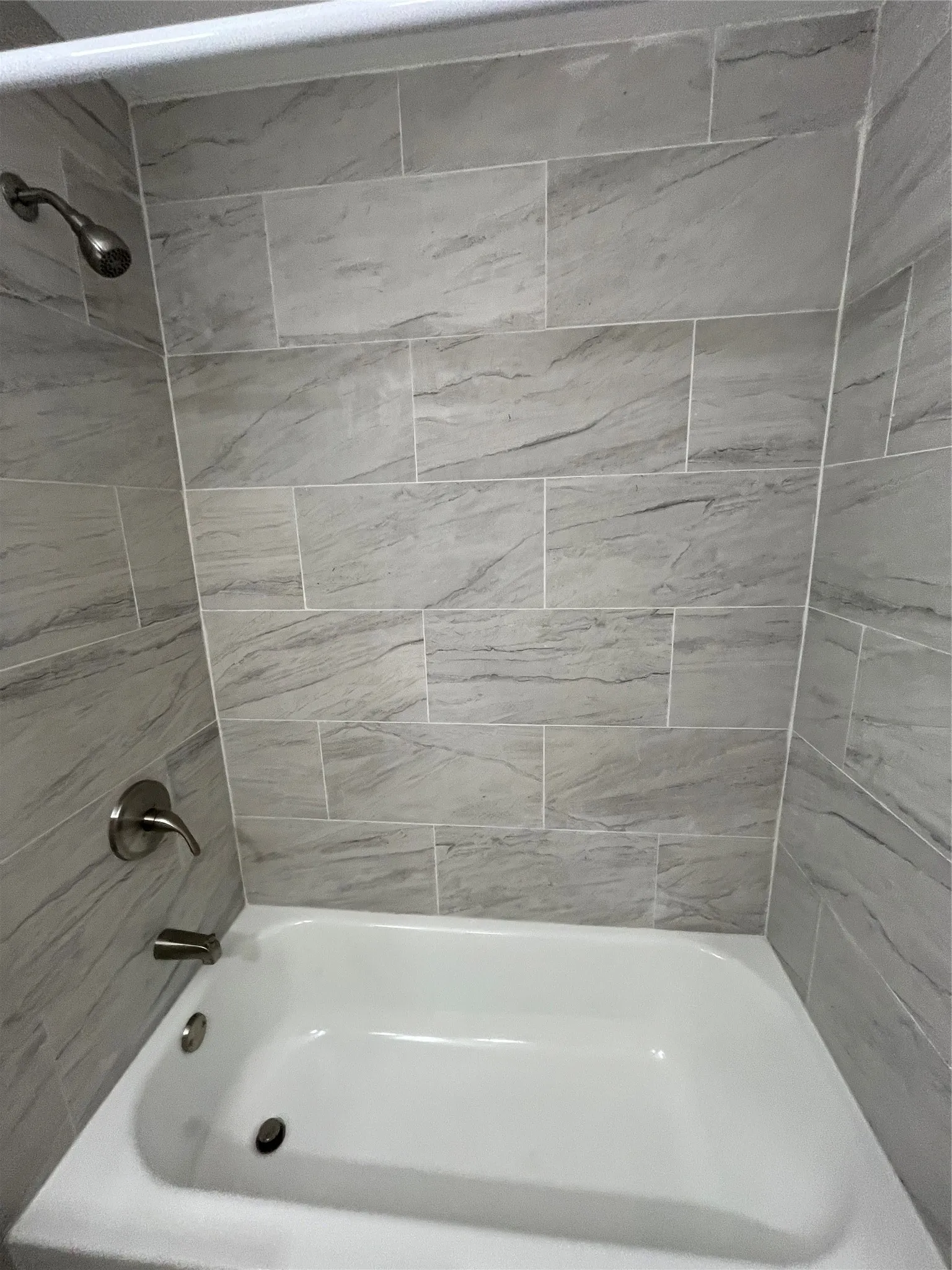 White bathtub with brushed nickel fixtures and gray-toned tile surround