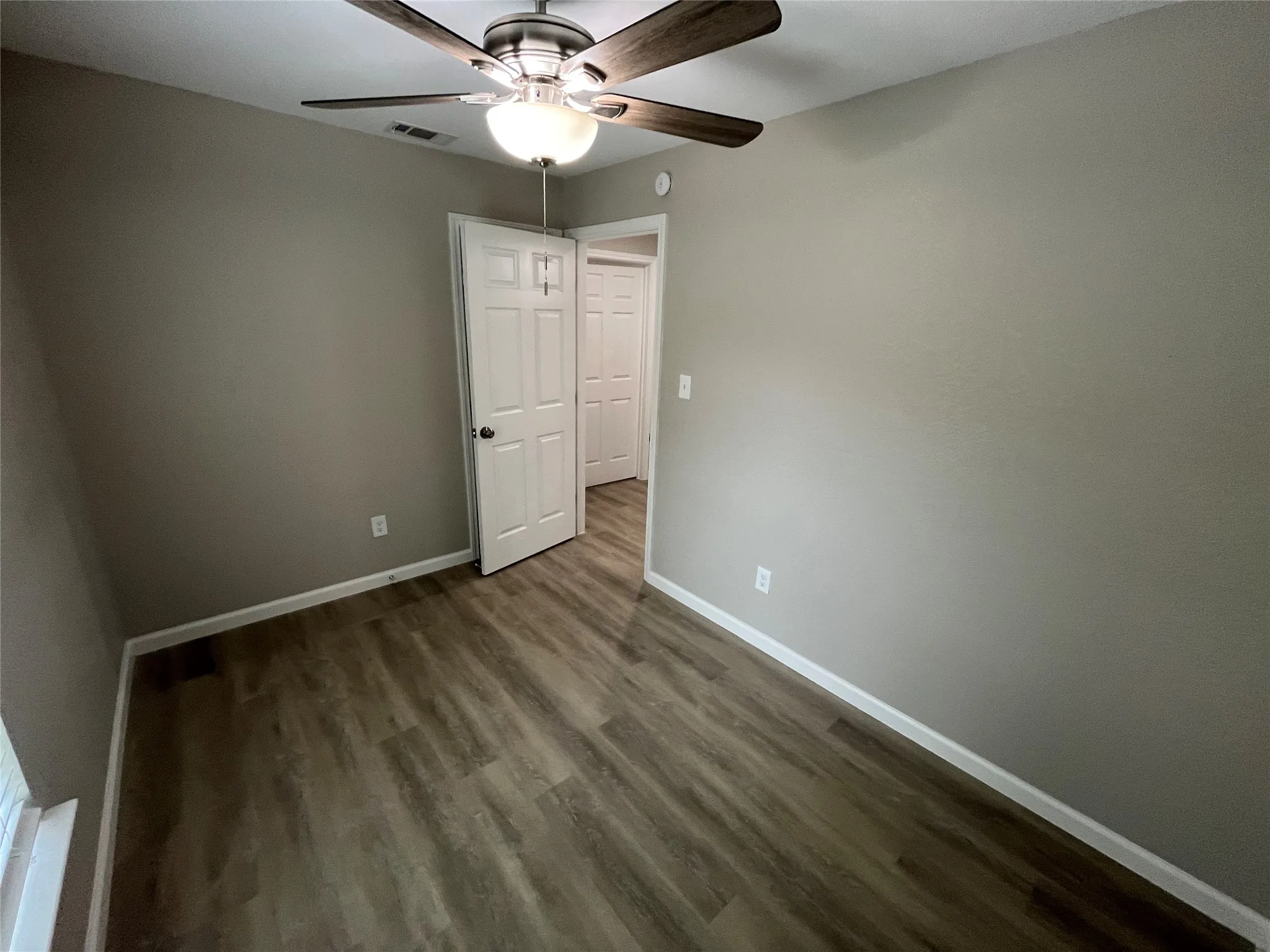 Wood-finish flooring, neutral wall paint, and a ceiling fan with integrated lighting