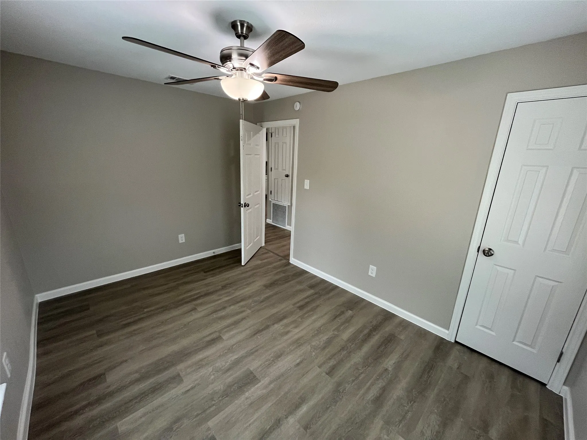 Wood-finish flooring with neutral wall tones, white trim, and a ceiling fan with light fixture