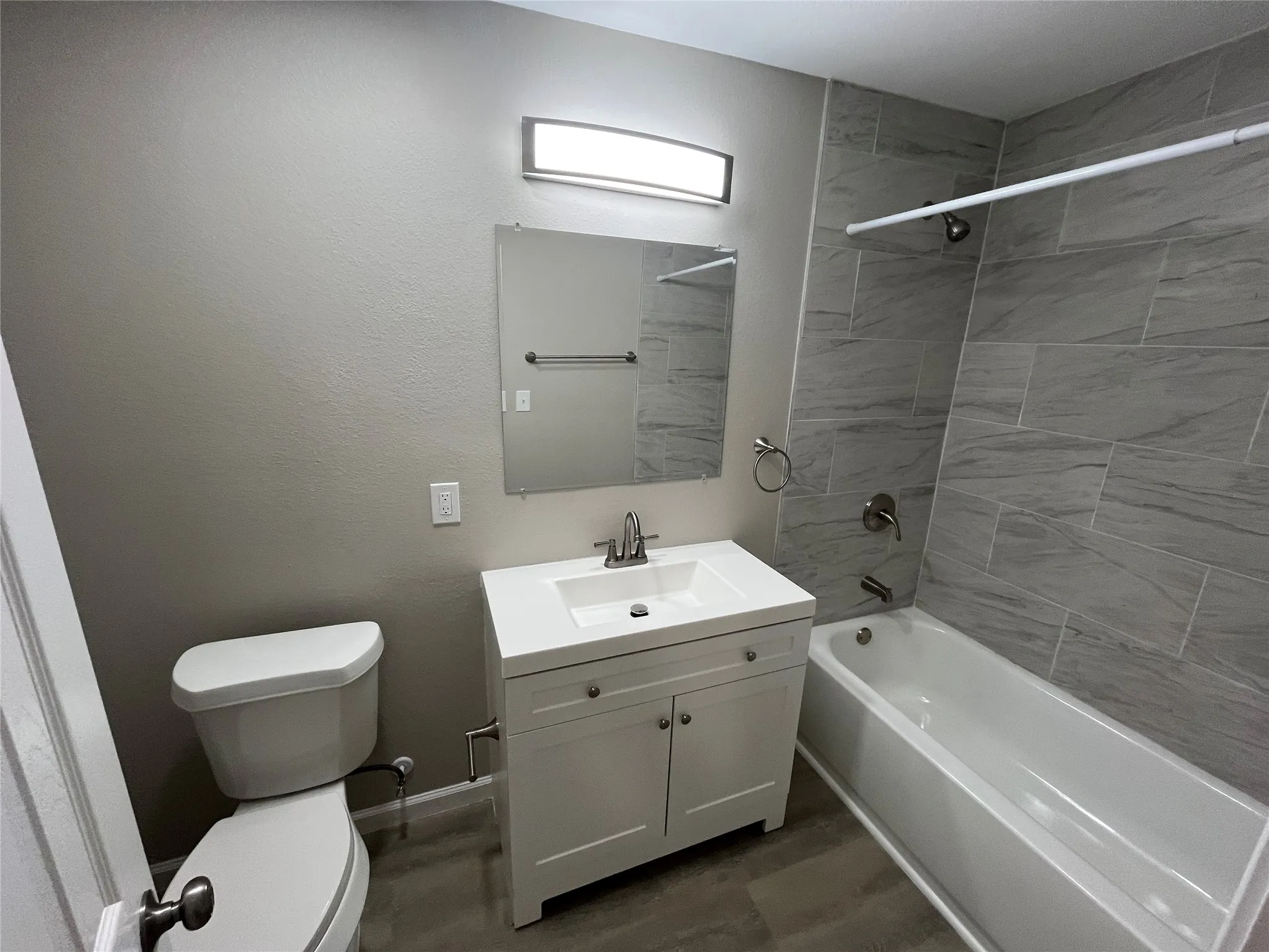 White vanity with integrated sink, rectangular mirror, brushed nickel fixtures, and light gray wall tile in the bath surround