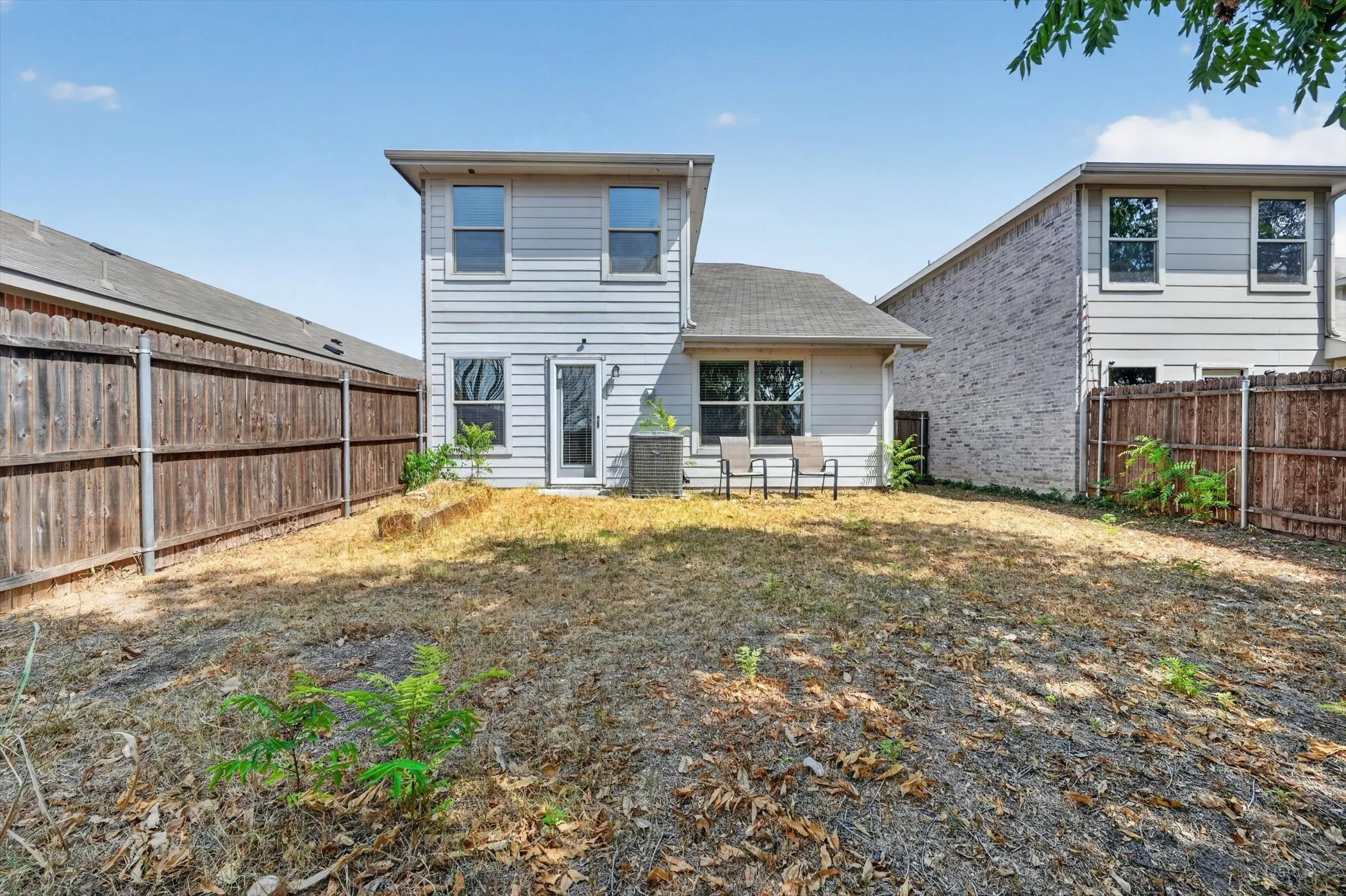 Rear view of the two-story brick home showing the back wall architecture, windows, and surrounding wooden privacy fence.