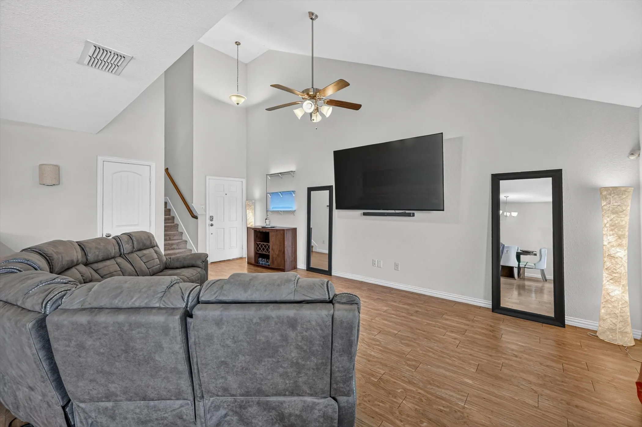 An open-concept living area with dark wood flooring, high ceilings with a ceiling fan, wall-mounted television, and direct sightlines to the kitchen and dining spaces.