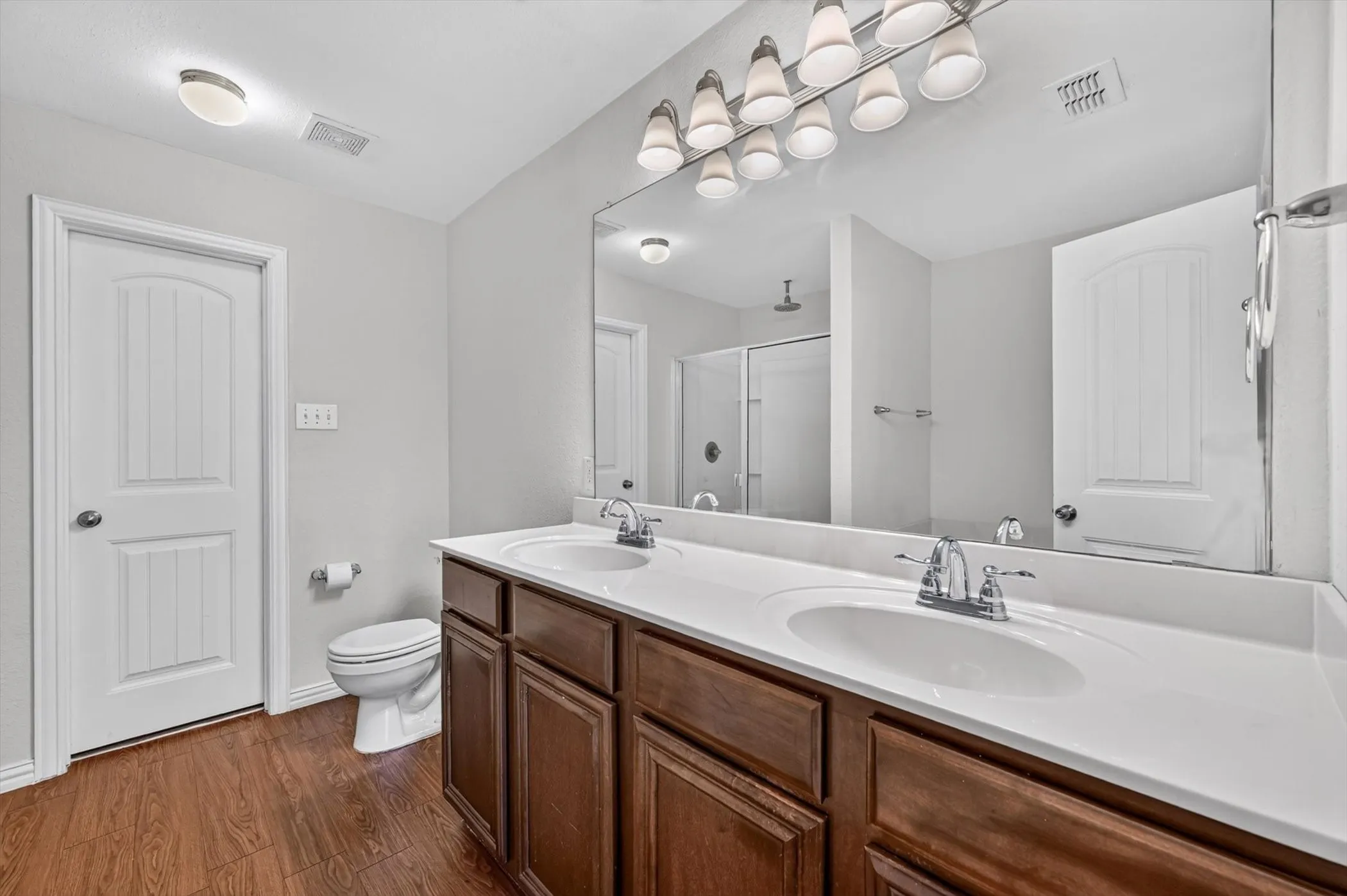 Primary bathroom dual-sink vanity with dark wood cabinets, large vanity mirror, and modern light fixtures