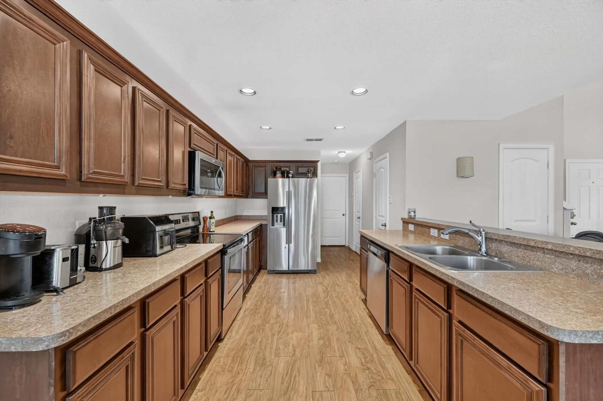 A modern kitchen equipped with dark wood cabinetry, tile floors, granite look counter space, stainless steel built-in microwave and stove, and functional pantry storage.