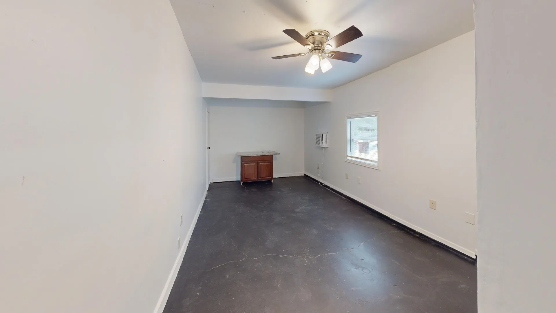 Ceiling fan, window, built-in wooden cabinetry, white walls, and dark flooring