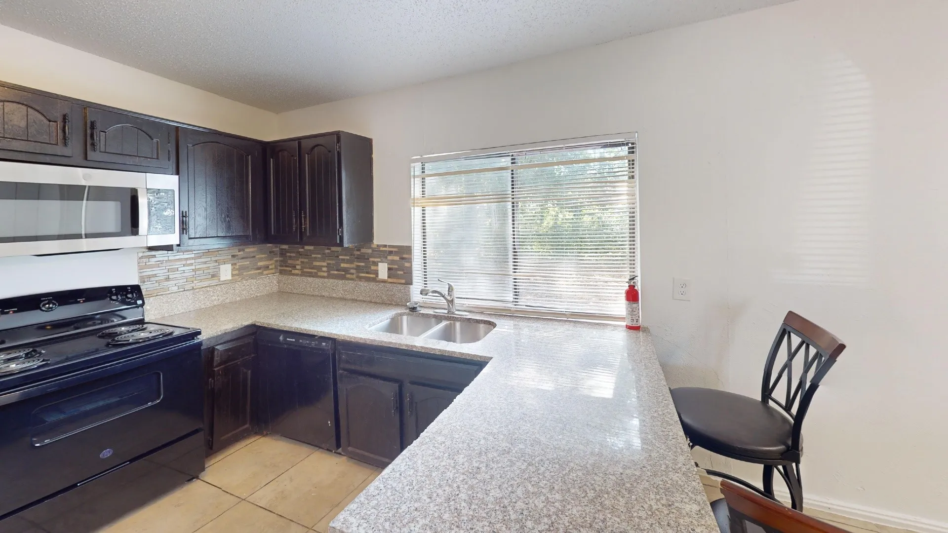 U-shaped counter with a dual basin sink, stainless steel microwave, black electric range, and dark wood-finish cabinetry