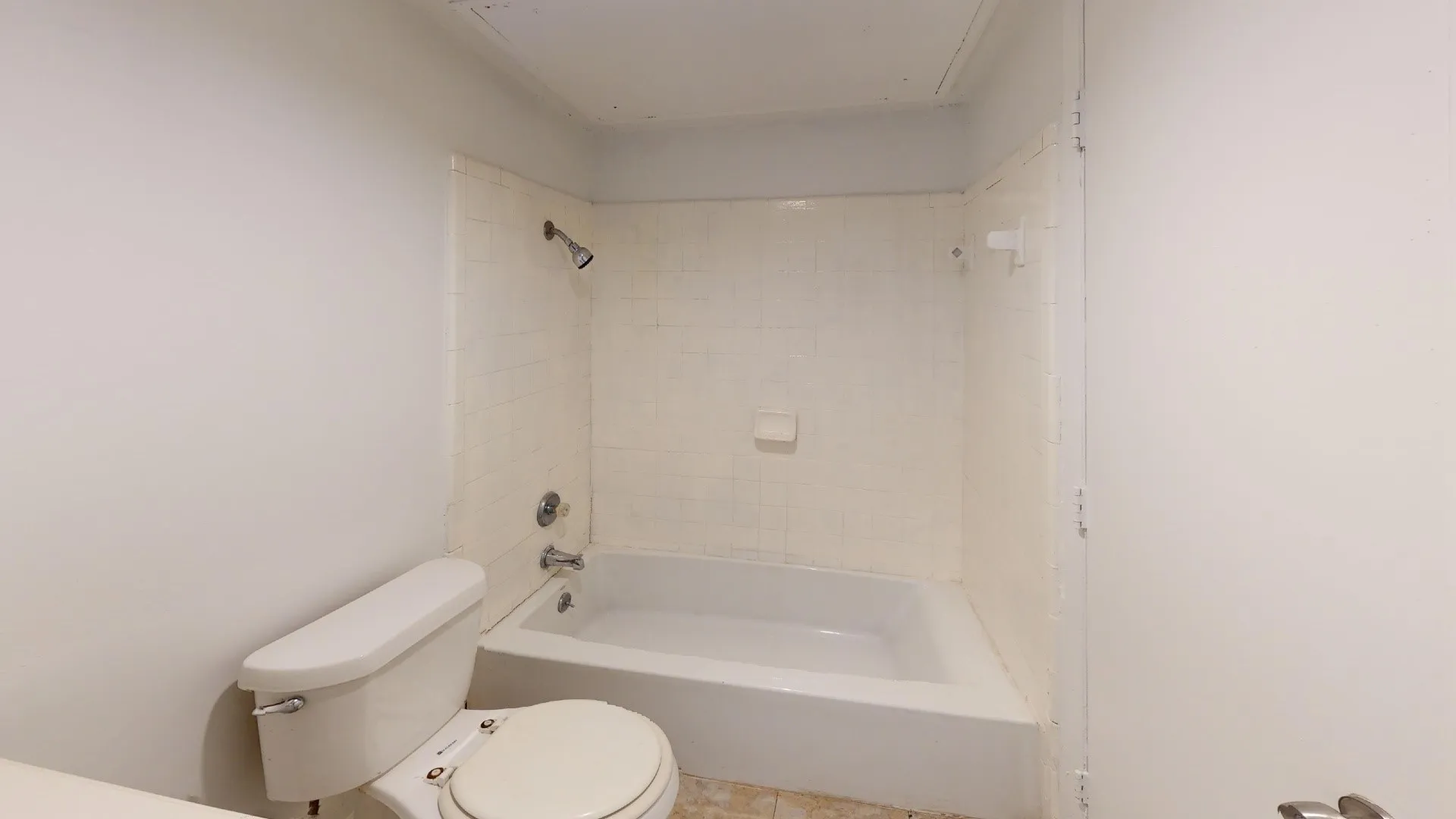White porcelain toilet and bathtub with tiled shower surround