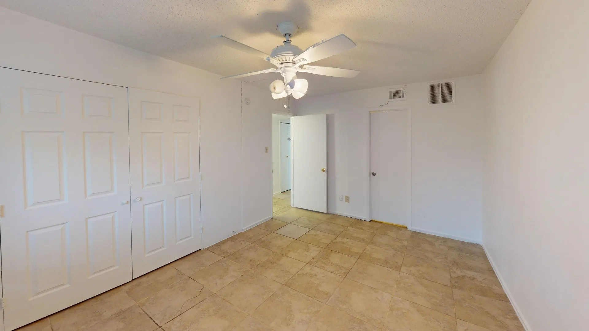 Tile flooring, white walls, ceiling fan with light fixture, white interior doors, and a white six-panel bi-fold closet door