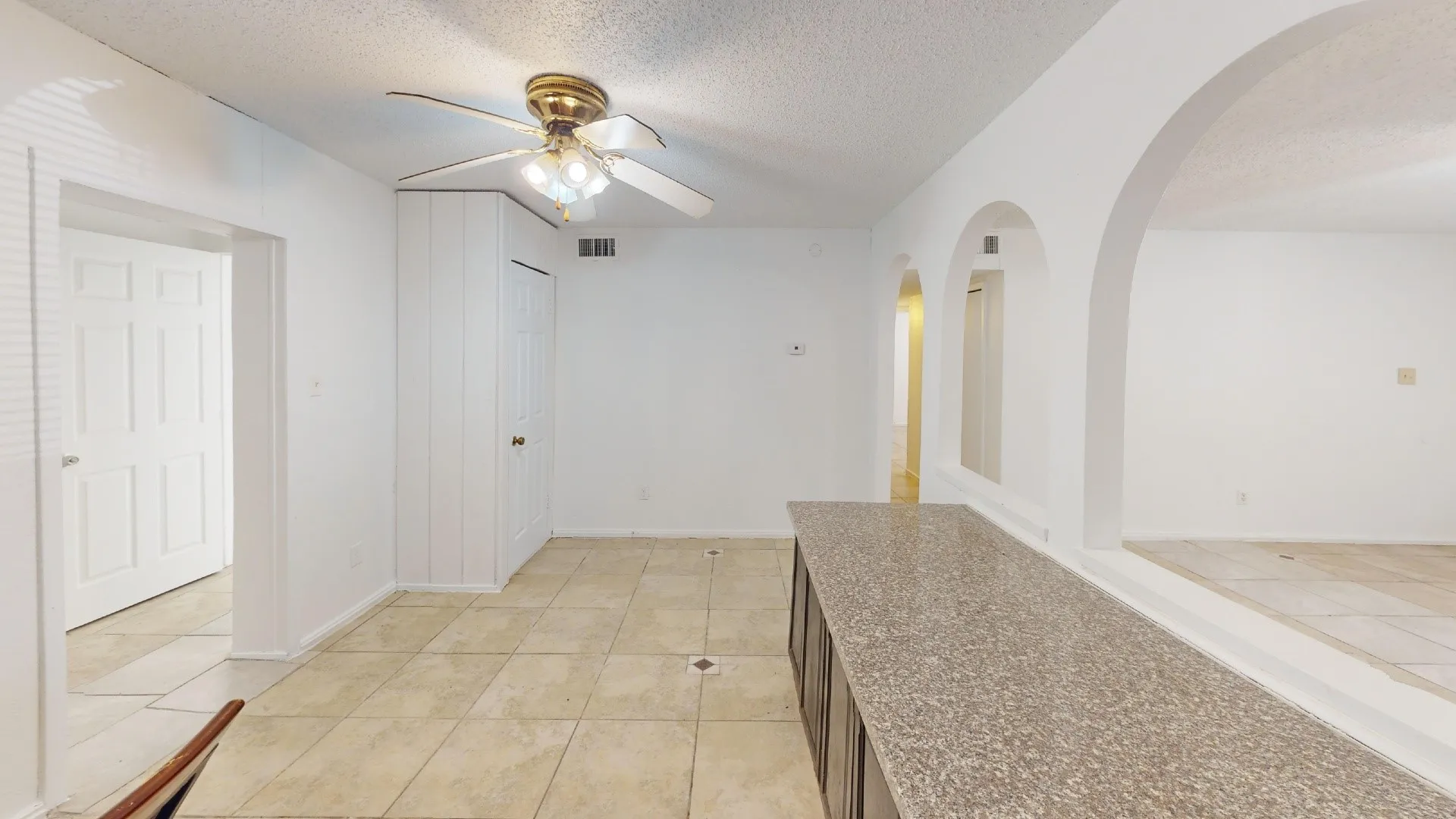 Tile flooring, built-in cabinetry with a stone-finish countertop, arched room openings, and a ceiling fan with integrated lighting