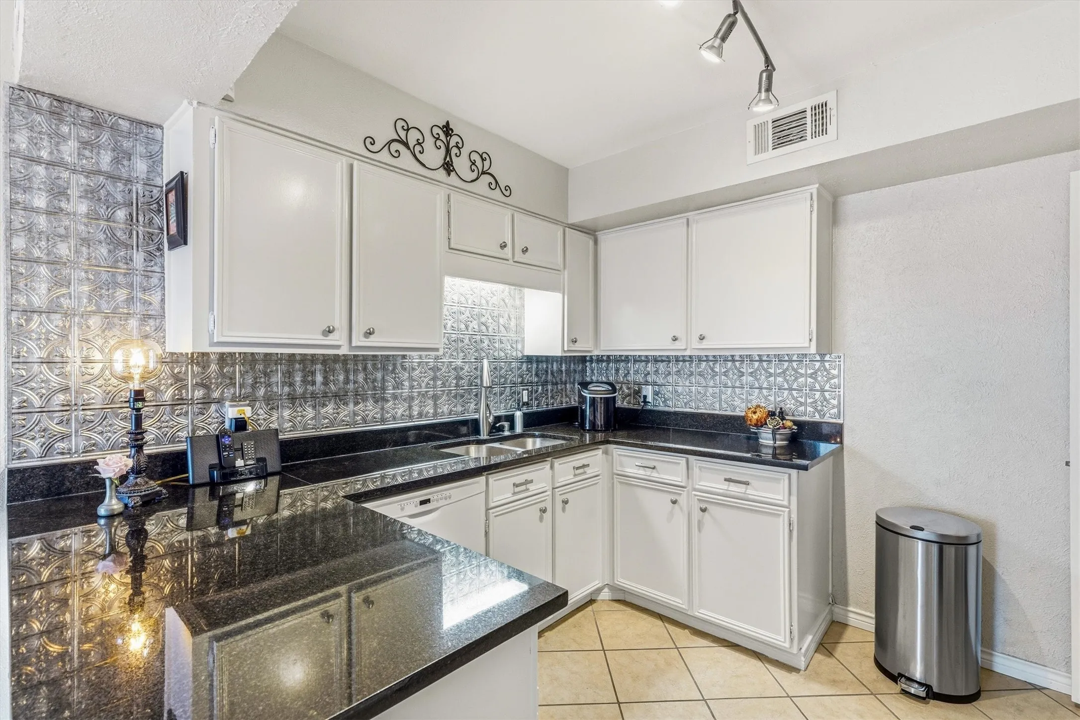 White cabinetry, dark stone countertops, tile backsplash, built-in sink, and tile flooring