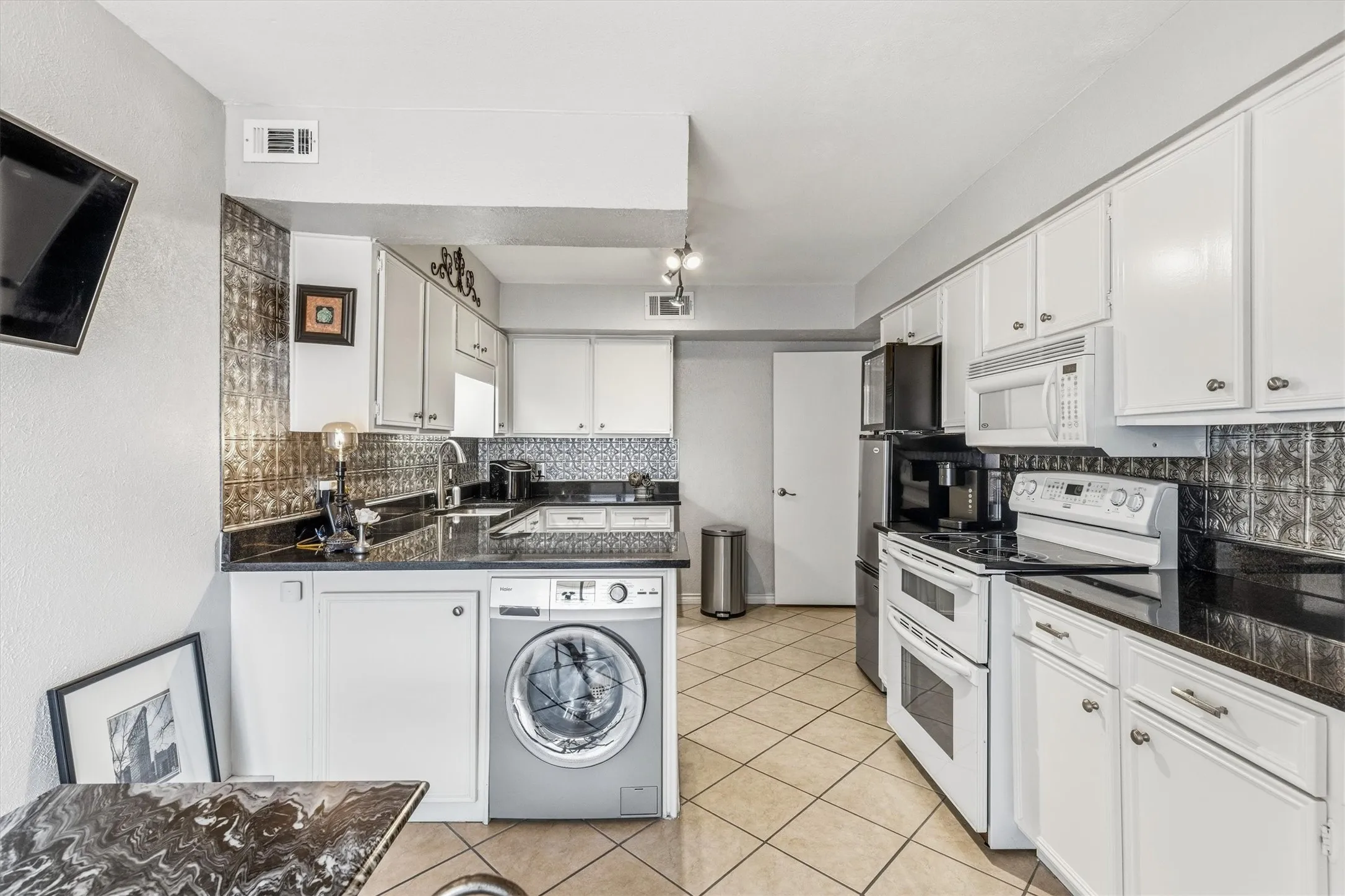 Kitchen featuring white cabinetry, dark countertops, a tile backsplash, and a built-in washing machine