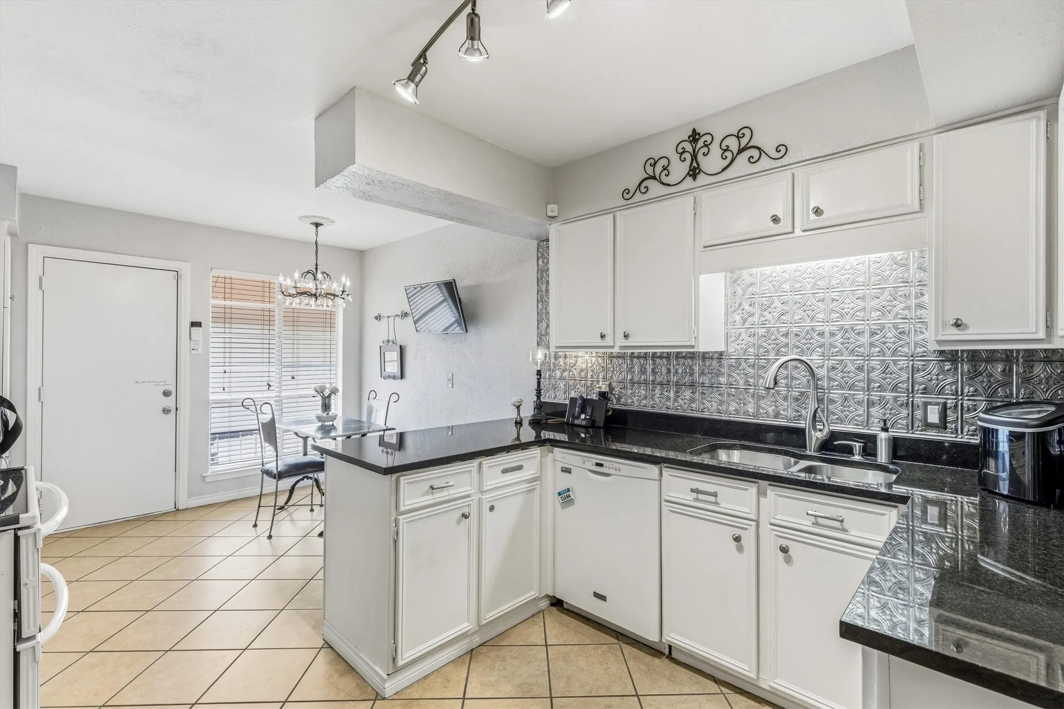 Kitchen featuring white cabinetry, dark countertops, a textured backsplash, stainless steel sink with a gooseneck faucet, and tile flooring