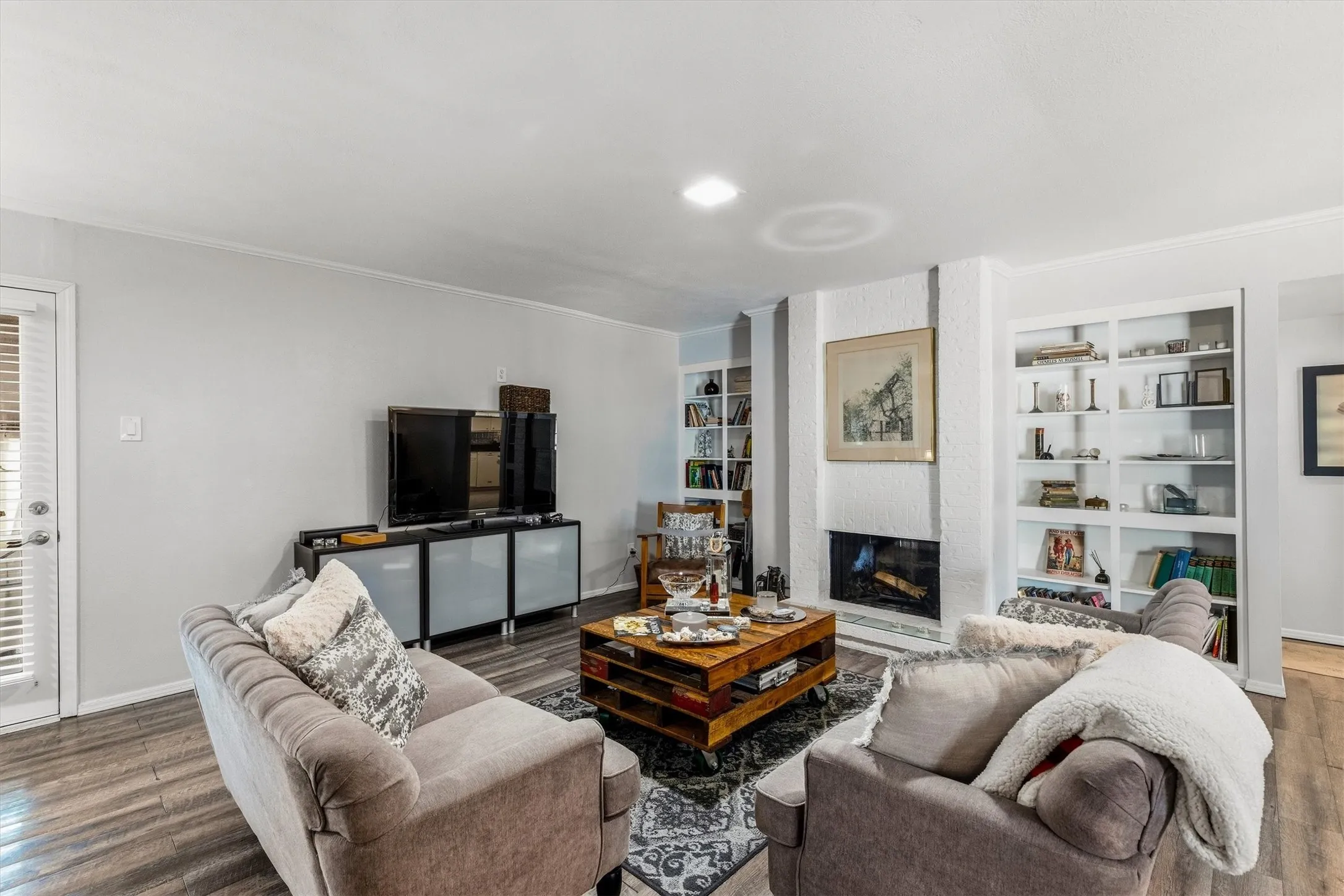 Wood-finish flooring, built-in shelving, recessed lighting, and a fireplace with a stone surround