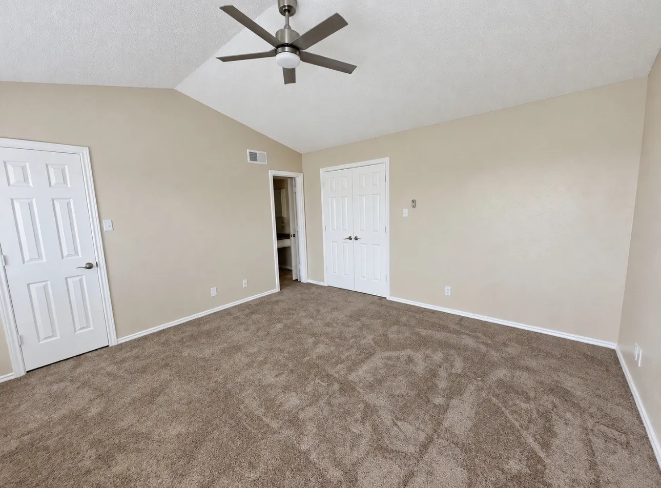 Vaulted ceiling, ceiling fan, neutral carpet, white paneled doors, and light-toned walls