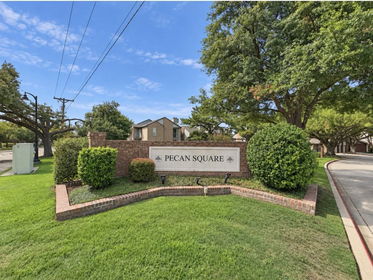 Brick-faced monument sign with "Pecan Square" lettering, surrounded by manicured landscaping, and mature trees