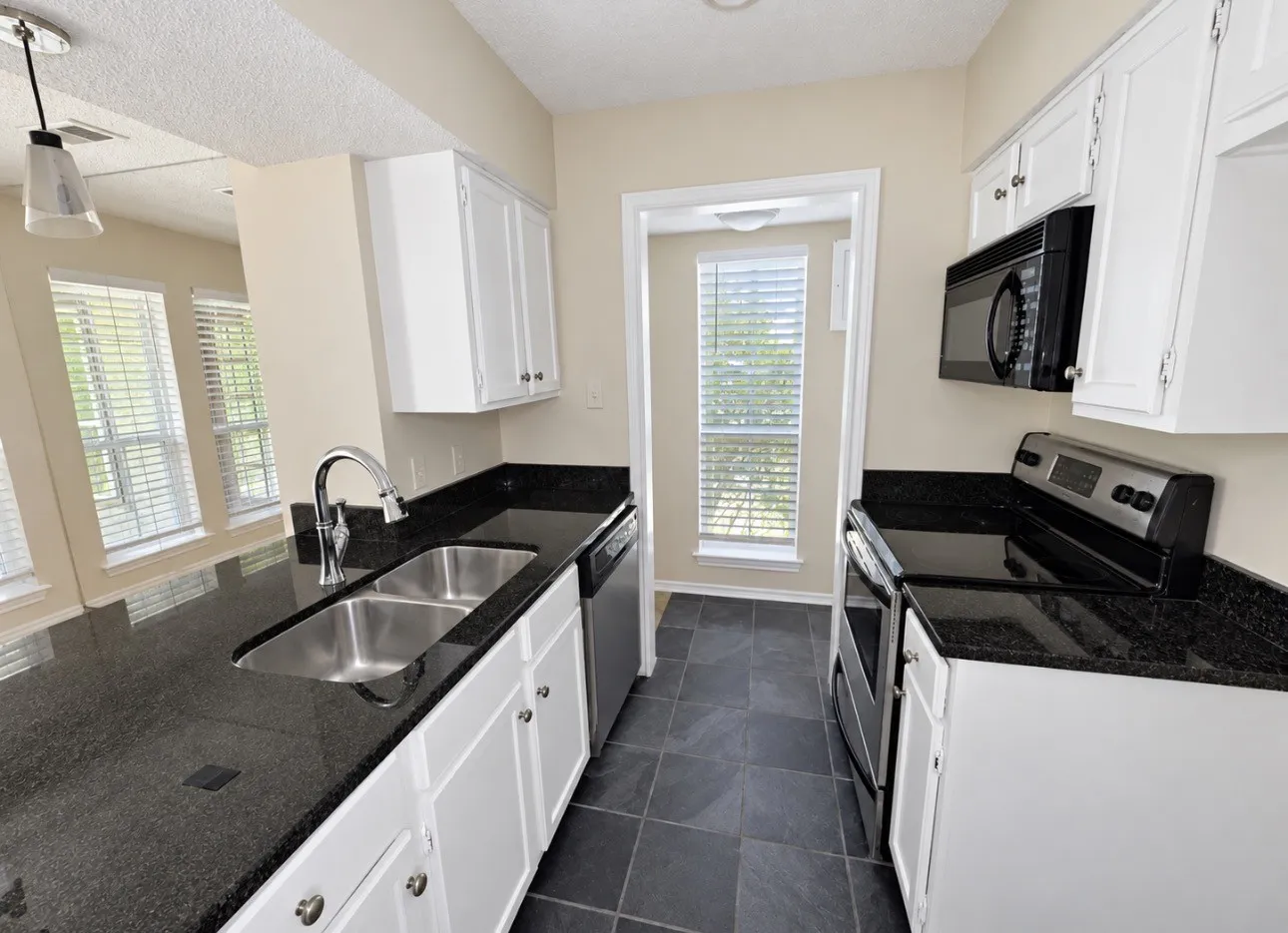 Kitchen featuring white cabinetry, dark countertops, stainless steel dual basin sink, and dark floor tiles