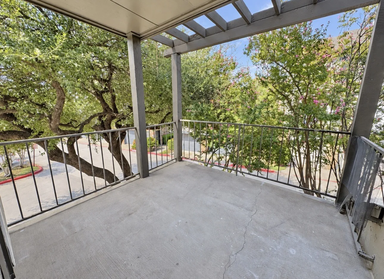 Concrete surface balcony with black metal railings and a pergola ceiling structure
