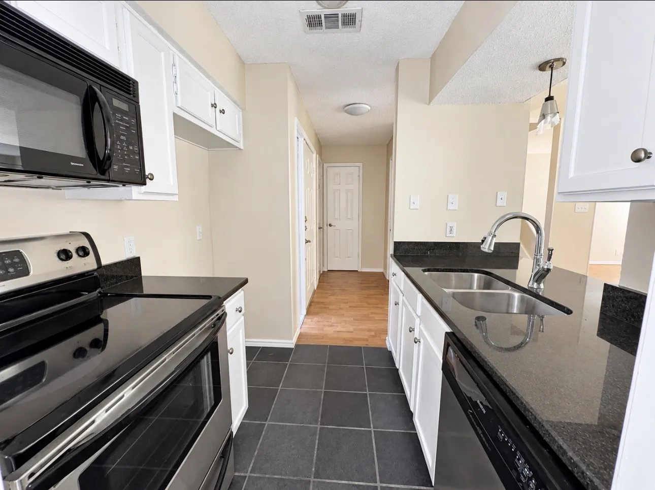 Kitchen featuring black tile flooring, white cabinetry with dark hardware, dark countertops, and stainless steel appliances