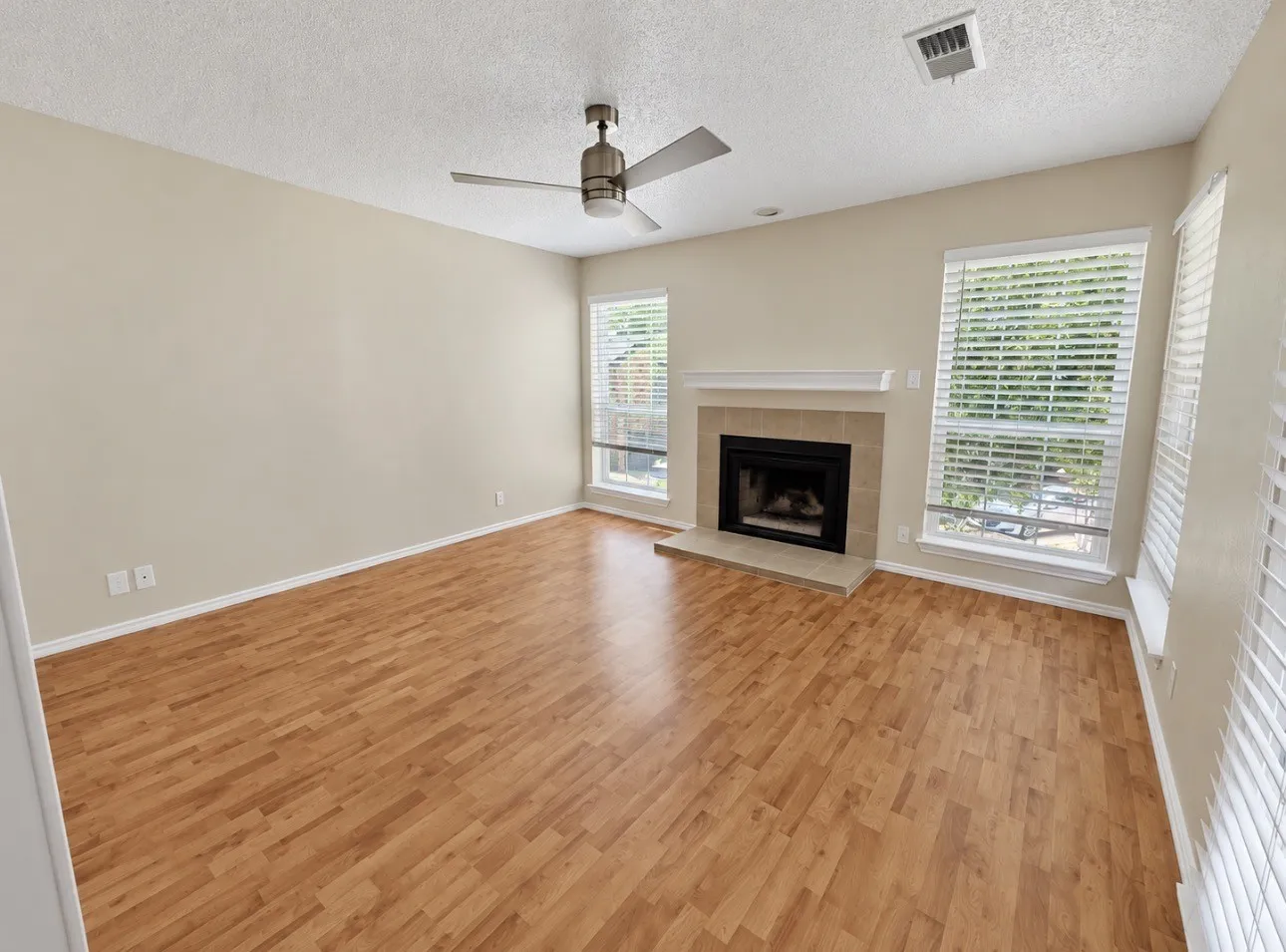 Wood-finish flooring, fireplace with stone surround and mantel, multiple windows, and a ceiling fan