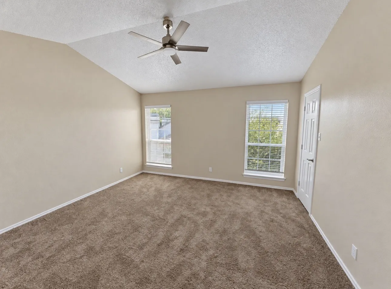 Vaulted ceiling with a ceiling fan, two windows with blinds, panel door, and brown carpet flooring