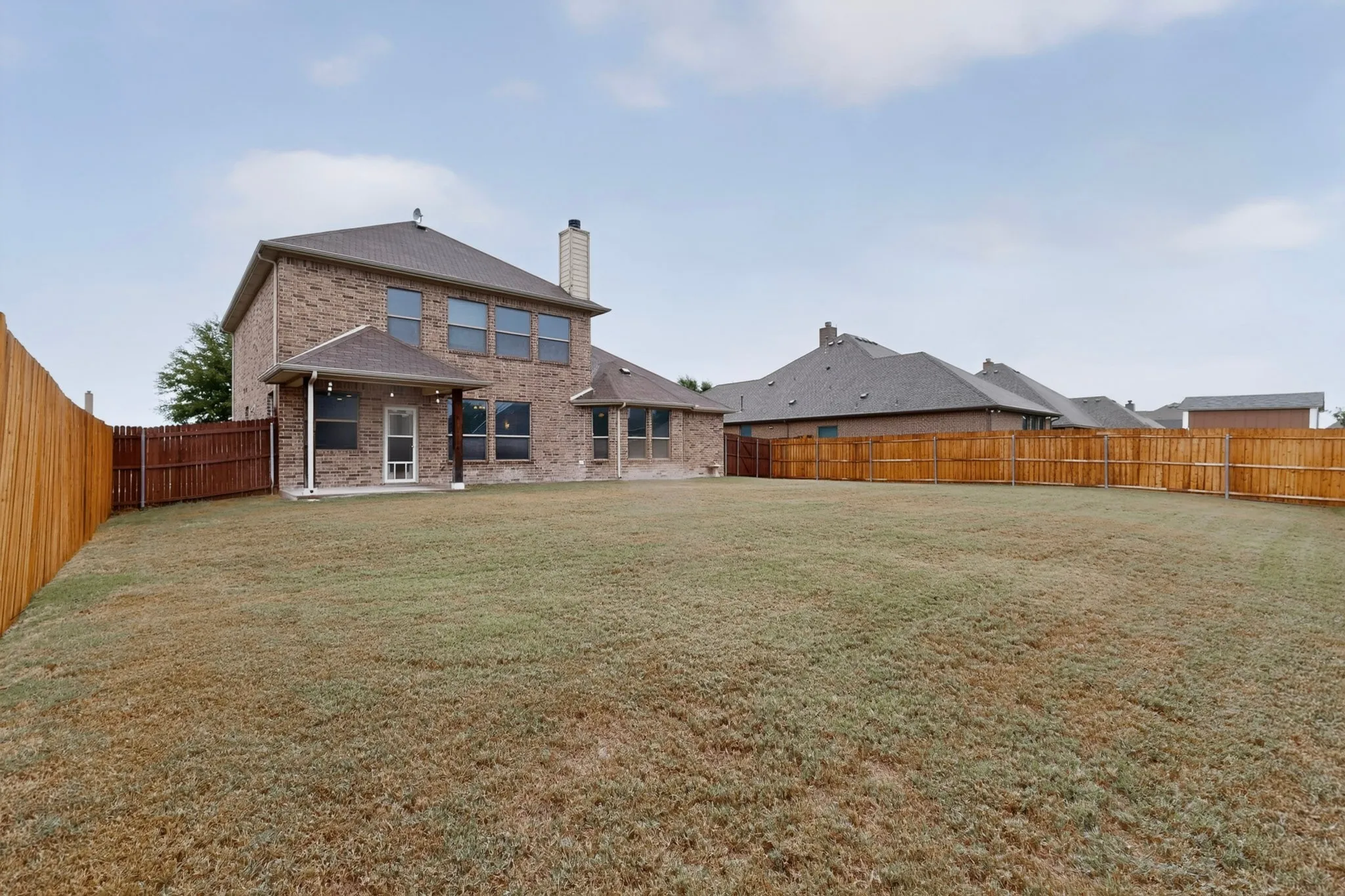 Expansive fenced backyard with a covered patio and brick exterior