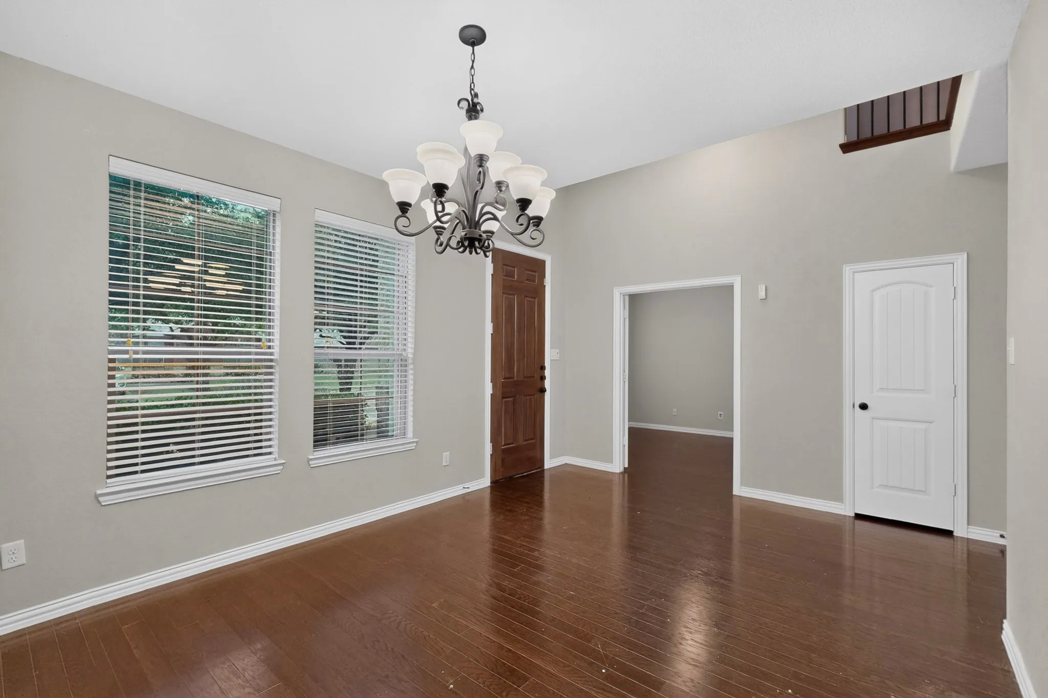 Wood-finish flooring, high ceilings, multiple windows, and an ornate chandelier