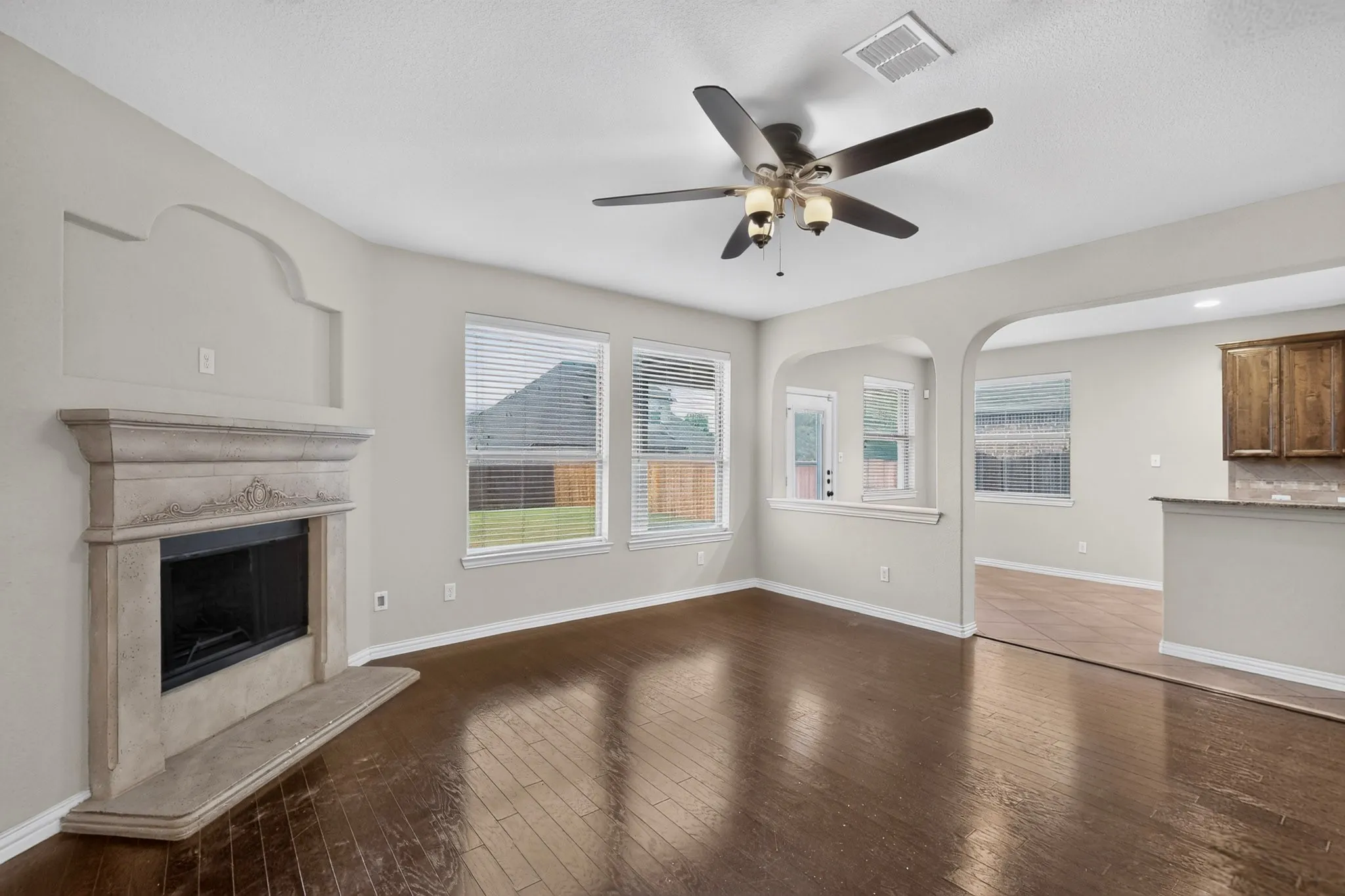 Fireplace with ornate mantel, wood-finish flooring, ceiling fan with integrated lighting, multiple windows, and arched entryways