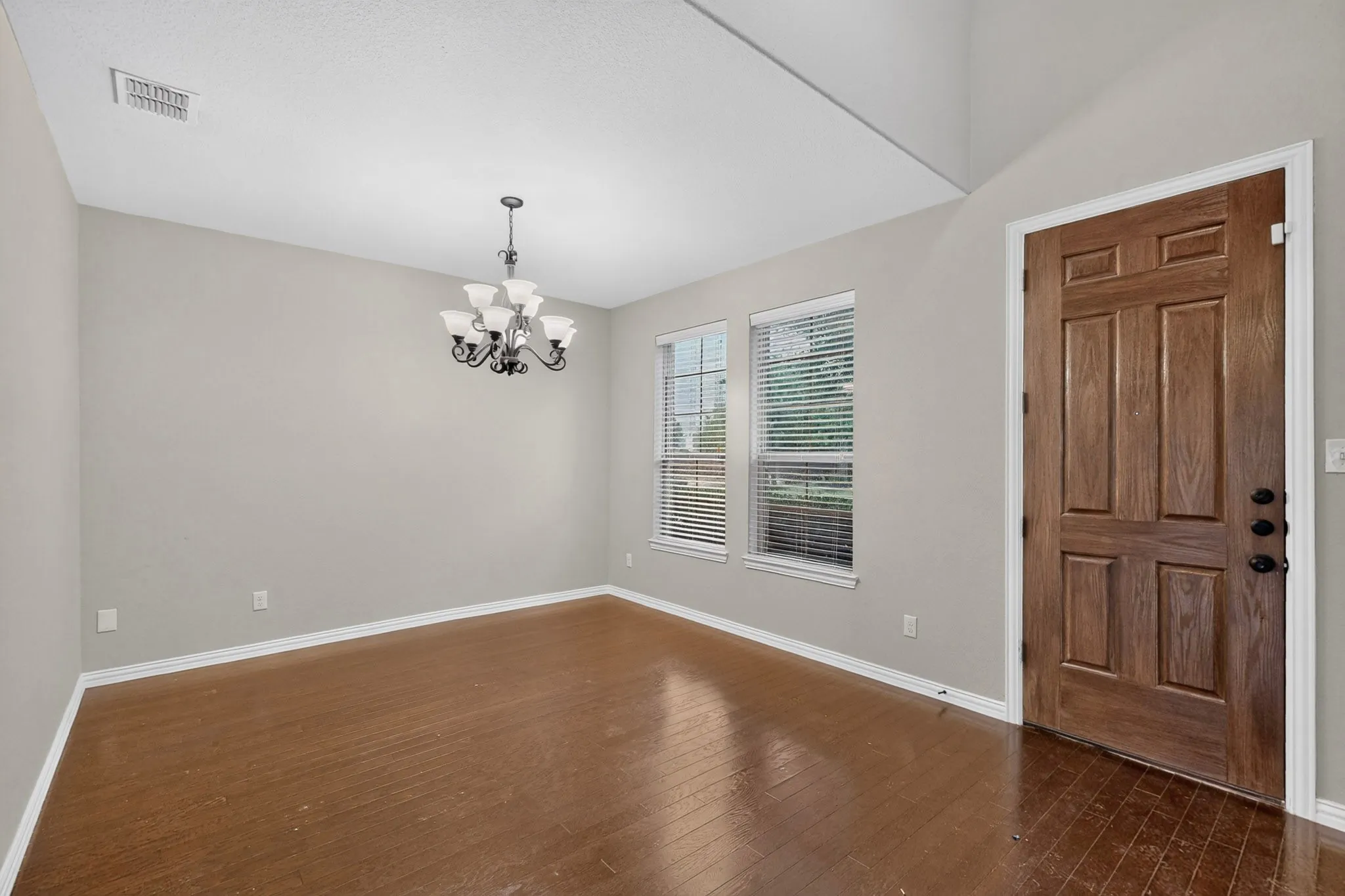 Wood-finish flooring, a paneled entry door, a classic chandelier, and multiple windows
