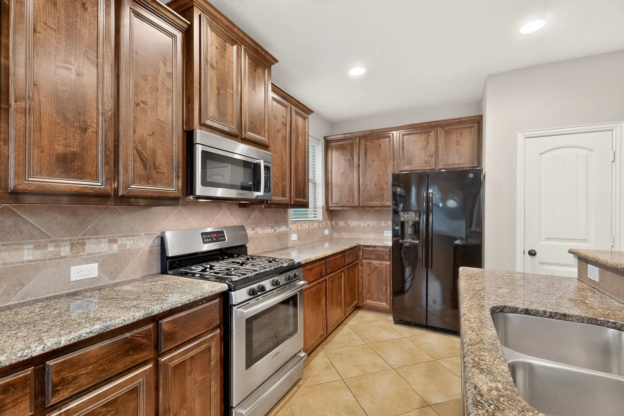 Full kitchen featuring wood cabinetry, granite countertops, tile backsplash, and stainless steel appliances