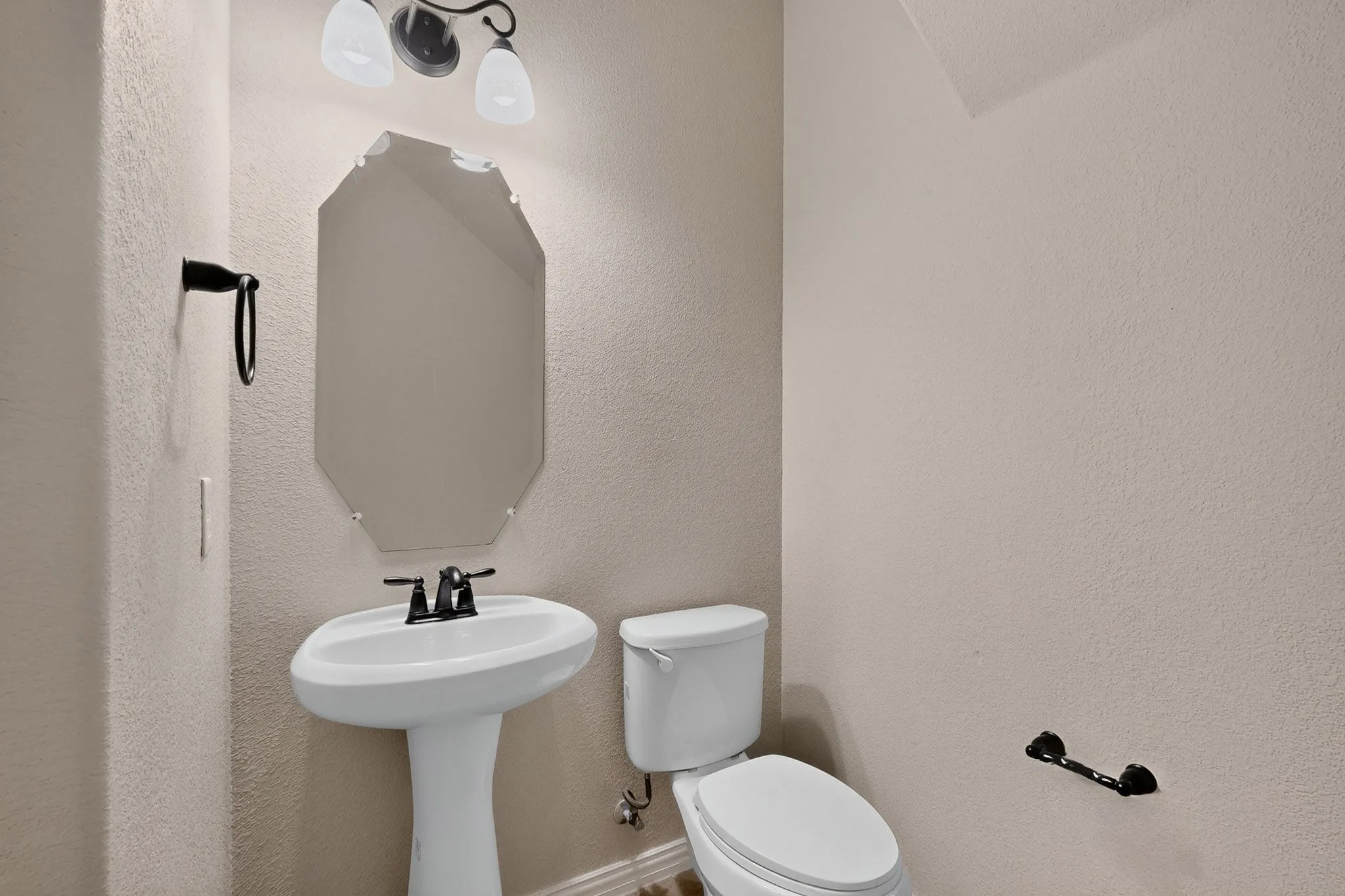 Pedestal sink with a dark-finish faucet, an octagonal frameless mirror, and a coordinating dark-finish light fixture