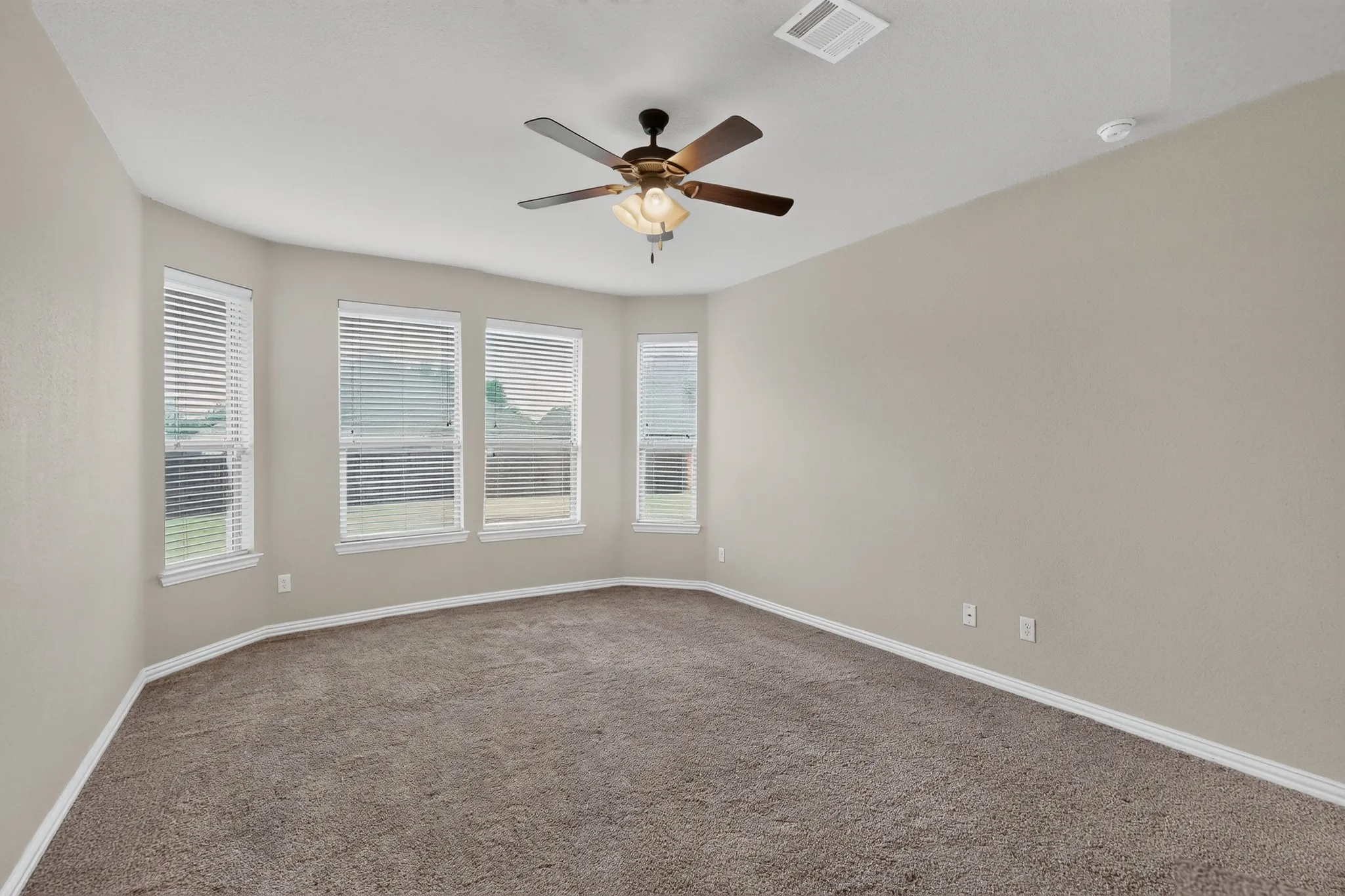 Curved wall with multiple windows, textured carpet, and a ceiling fan with integrated lighting