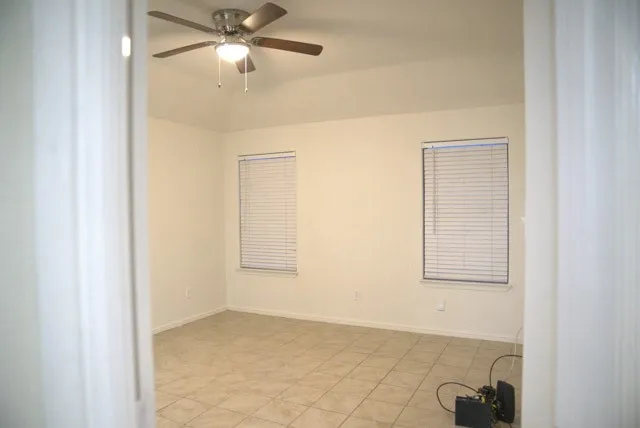 Vaulted ceiling featuring a ceiling fan with integrated lighting, two windows with blinds, and tile flooring