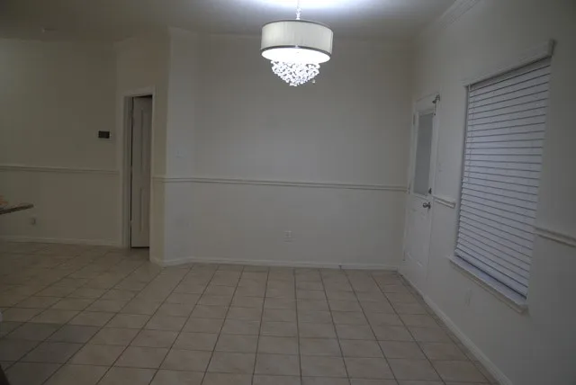 Tiled flooring, elegant drum chandelier, white paneled door, and crown molding
