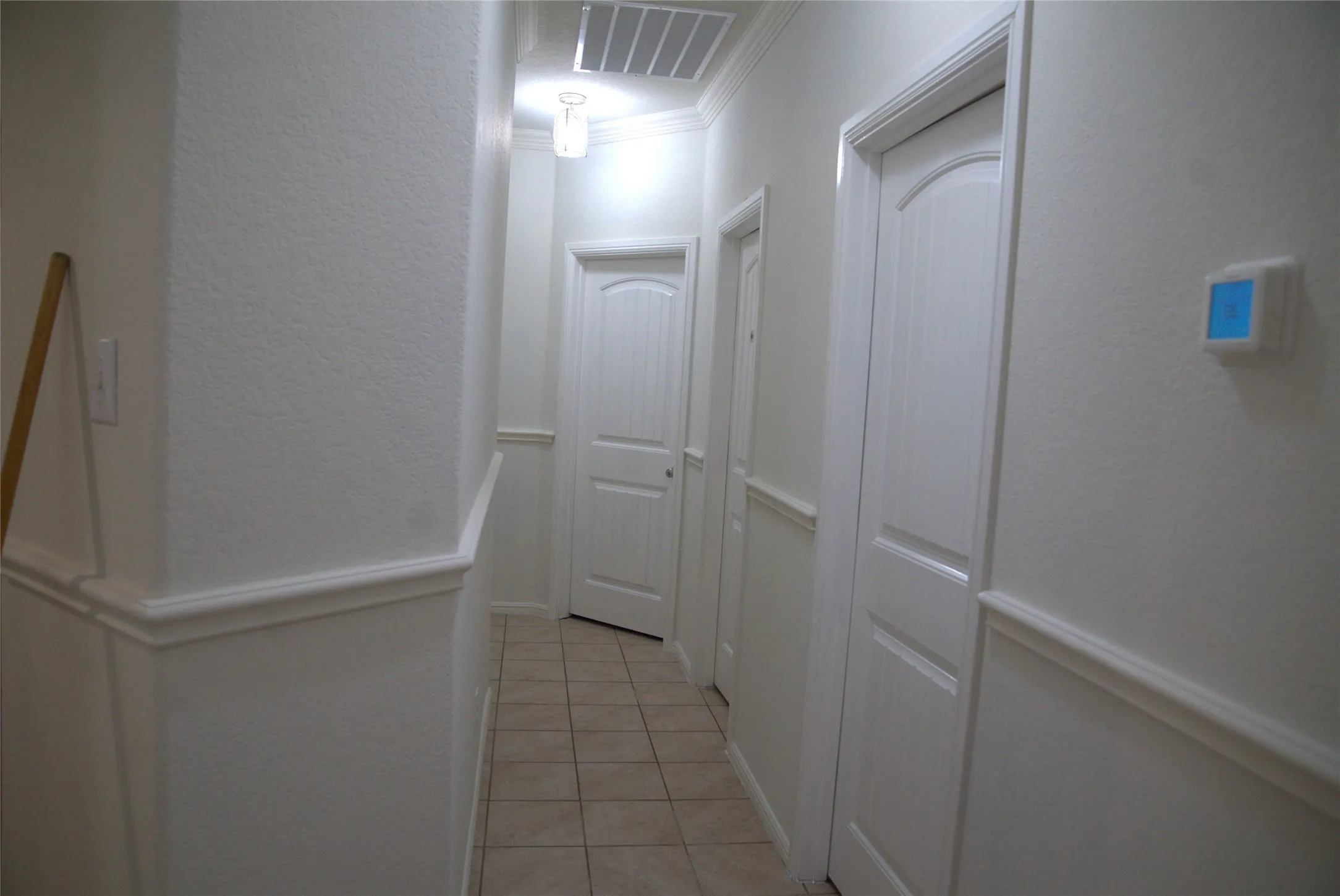 Hallway featuring tile flooring, white panel doors, chair rail molding, crown molding, and a flush mount ceiling light