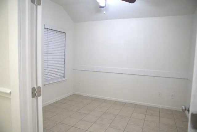 Vaulted ceiling featuring a ceiling fan, window with blinds, and tile flooring