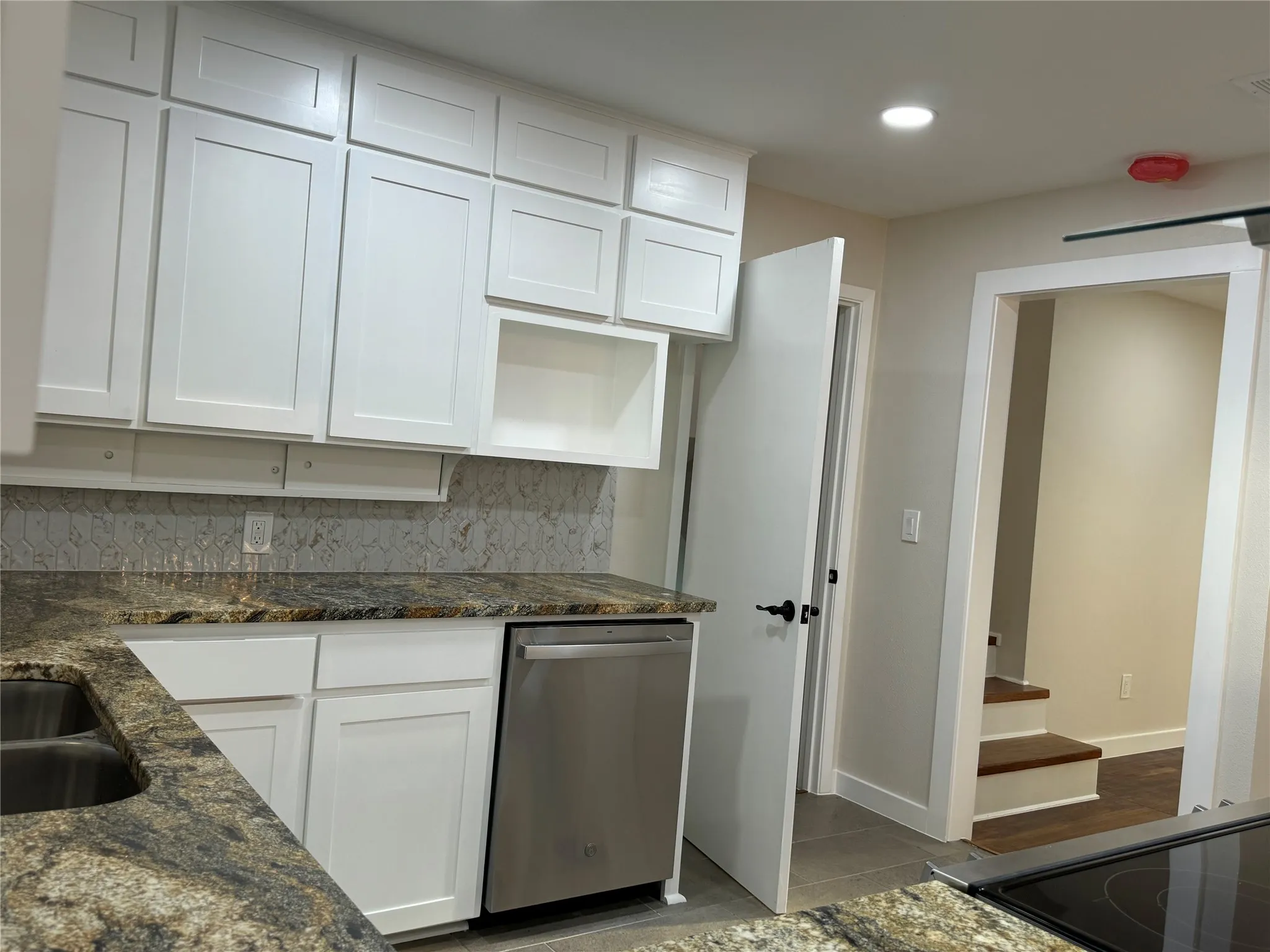 Kitchen featuring dark stone counters, white cabinetry, stainless steel dishwasher, and backsplash