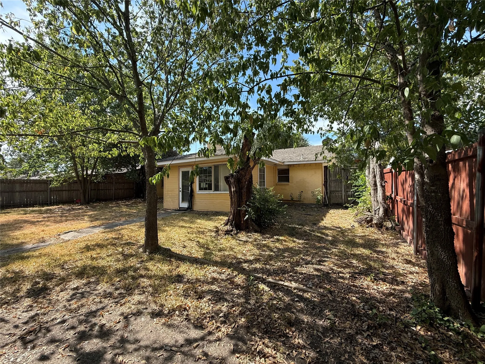 Expansive backyard featuring mature trees, partial fencing, and a stucco exterior