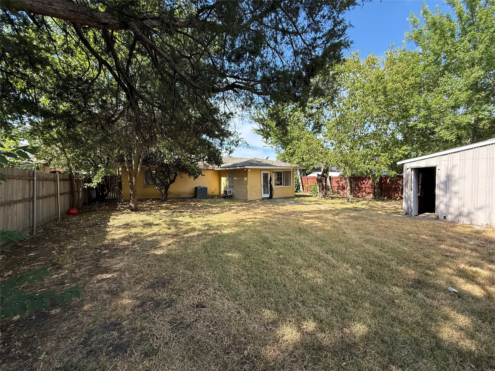 Expansive backyard featuring mature trees, a detached storage shed, and perimeter fencing